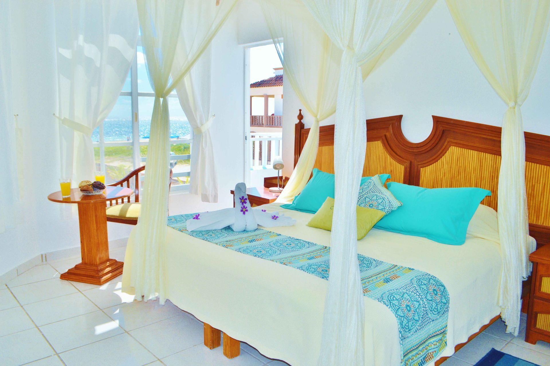 Dormitorio con cama con dosel, vista al mar. Colores turquesa y crema, muebles de madera.