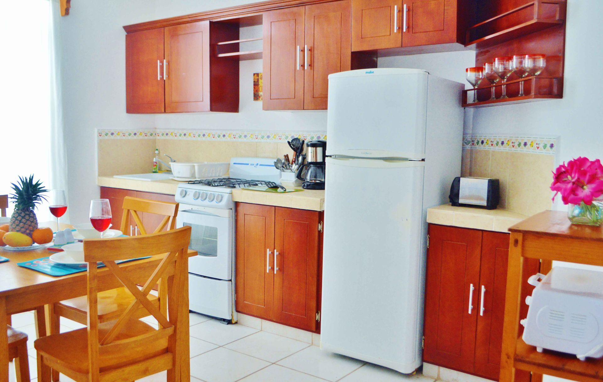 Cocina con armarios de madera, electrodomésticos blancos y mesa de comedor puesta con comida y bebidas.