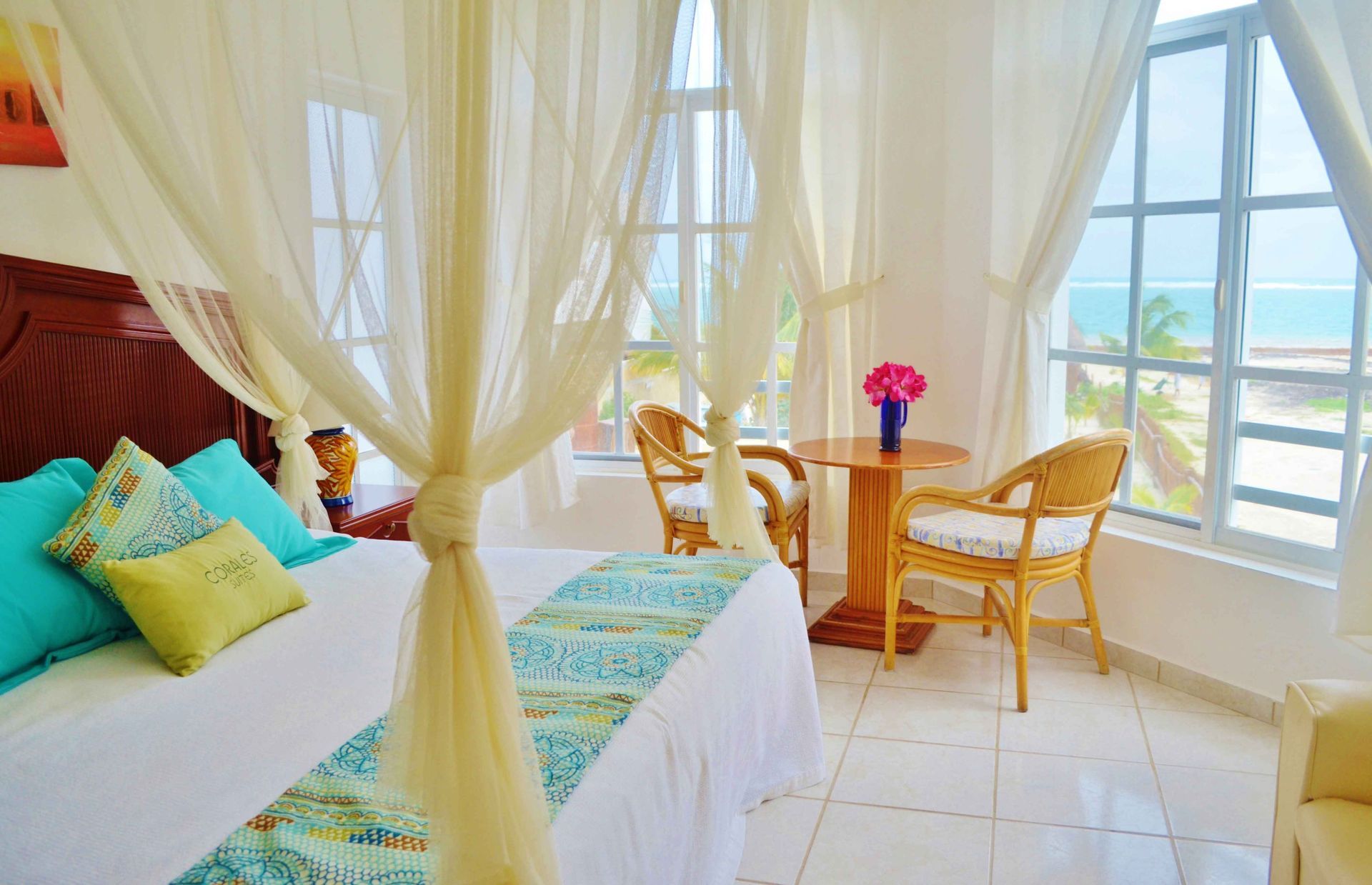 Dormitorio con cama con dosel, sillas de mimbre, mesa y vistas al mar.