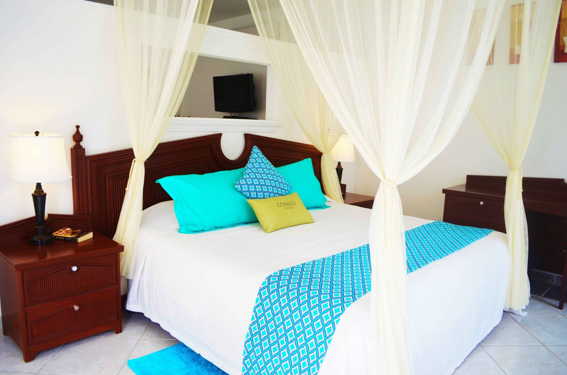 Bedroom with a canopy bed, turquoise and white bedding, wooden nightstands, and a mounted TV.