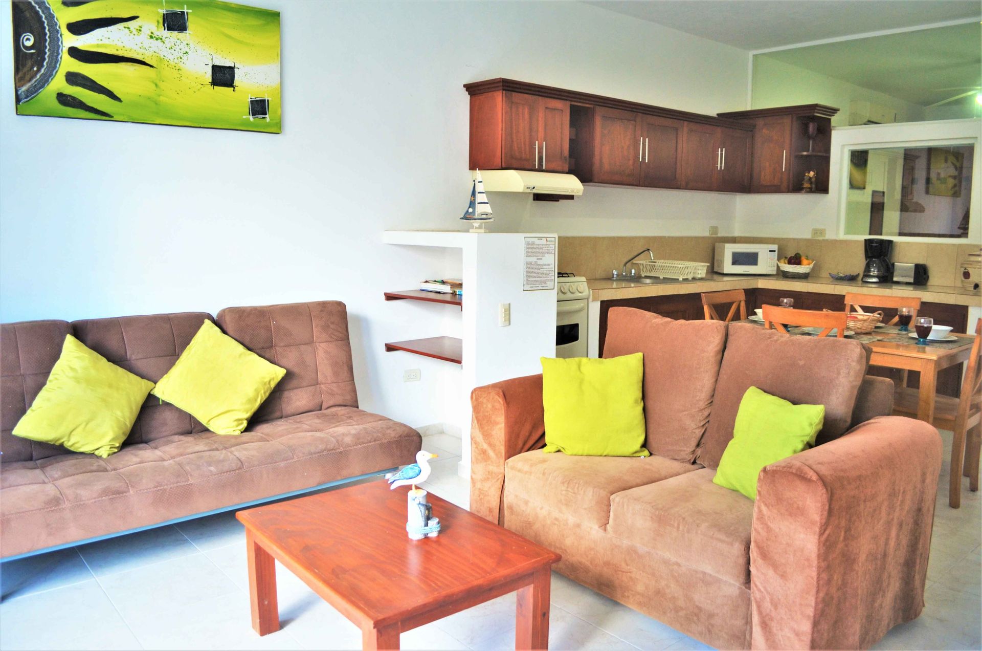 Living room with brown sofas, yellow pillows, a wooden table, and an open kitchen.