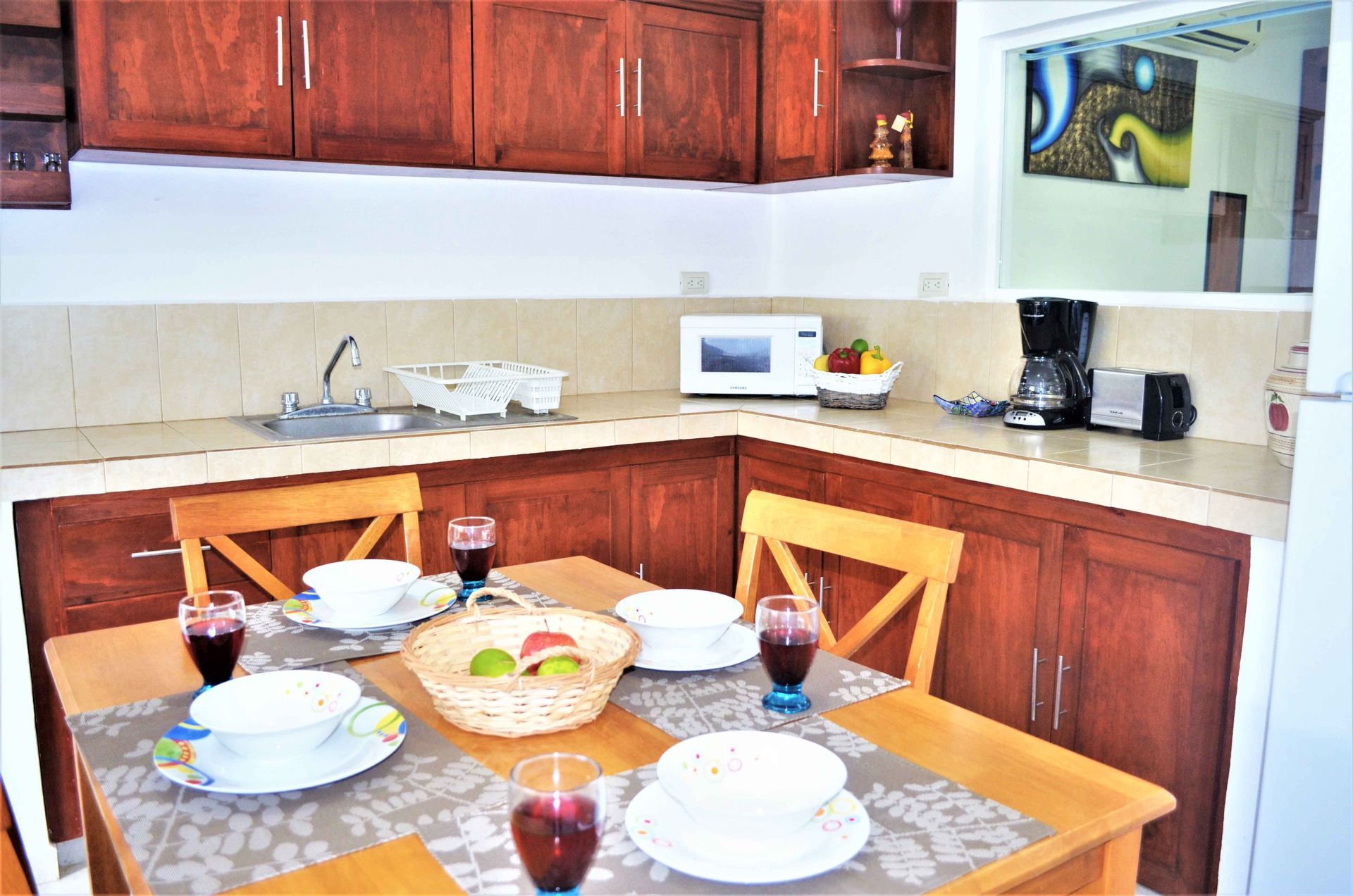 Kitchen with wooden cabinets, dining table set for four, fruit basket, microwave, and coffee maker.