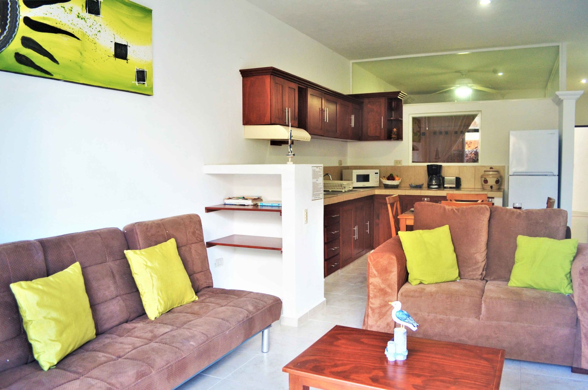 Living room with brown sofas, yellow pillows, open kitchen, and artwork.