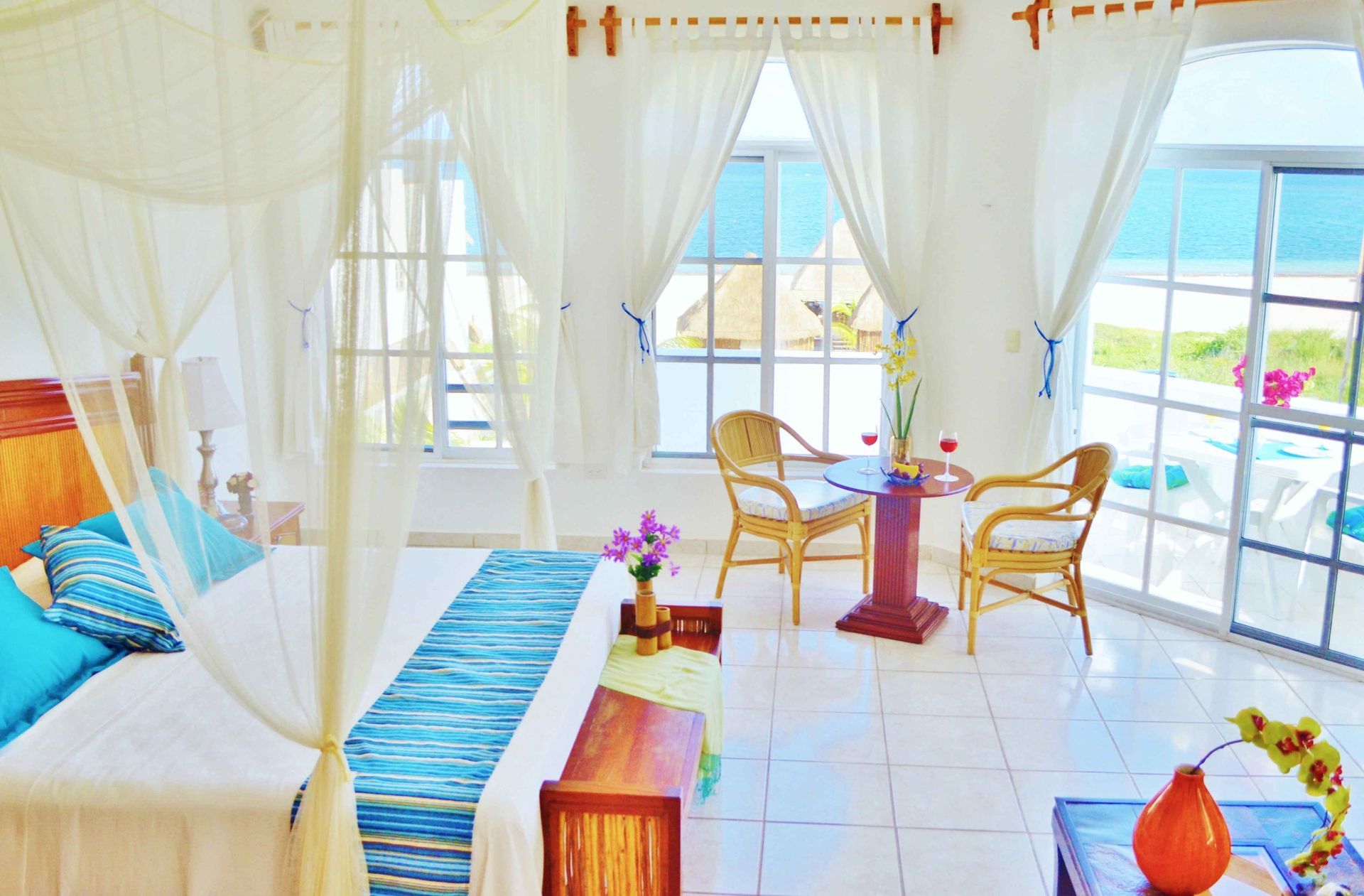 Bright white bedroom with a canopy bed, small table, and ocean view.