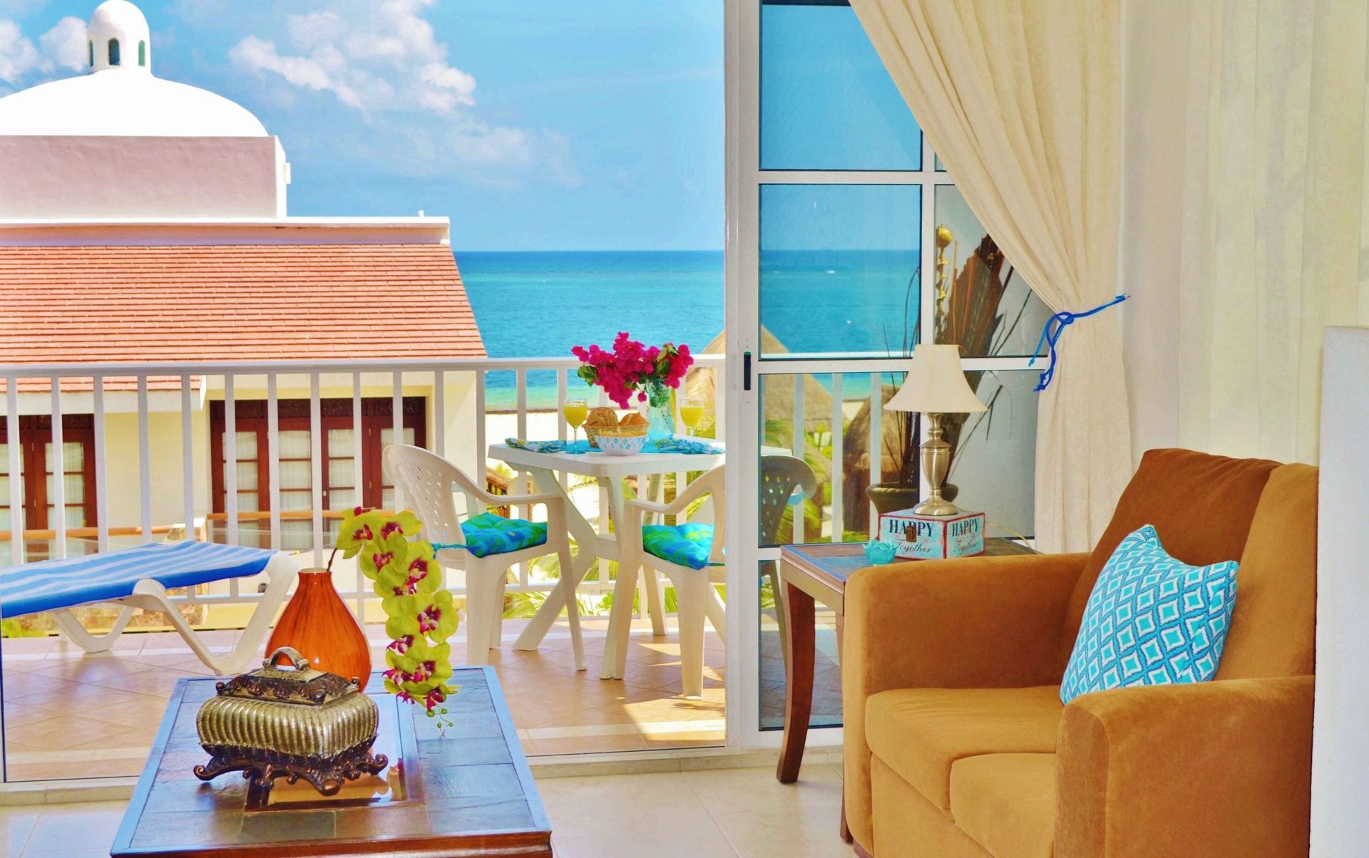 Coastal apartment with ocean view, brown sofa, balcony table with flowers.