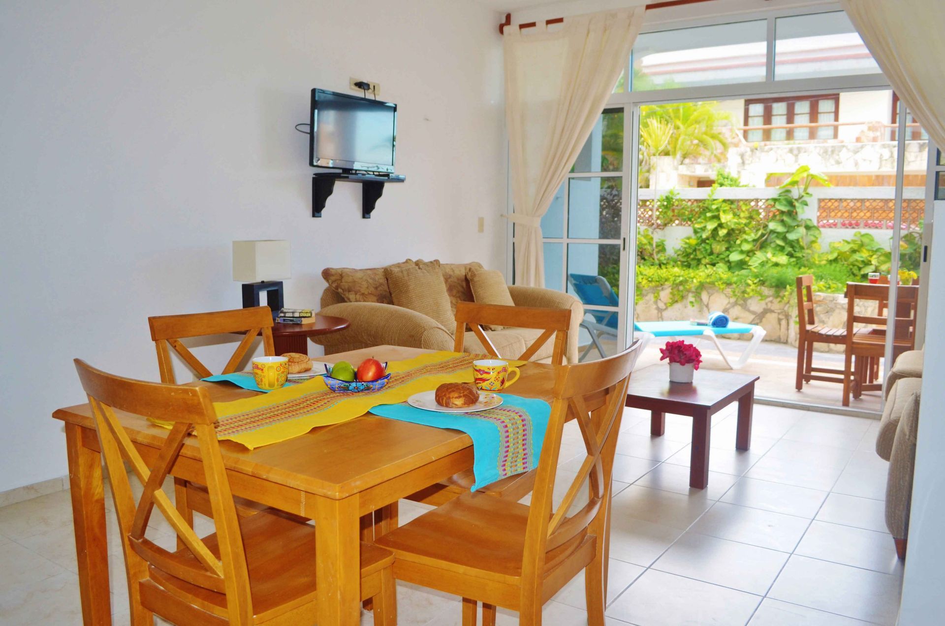Comedor con mesa puesta para comer, que da a un patio con plantas y piscina.