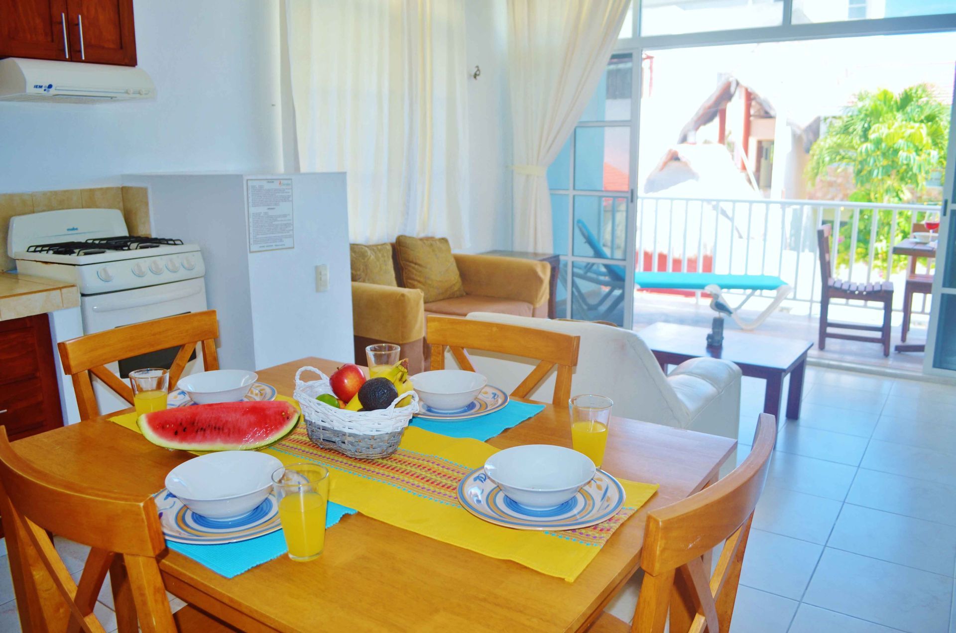 Comedor preparado para el desayuno, con acceso a un balcón. Cocina americana y sofá al fondo.