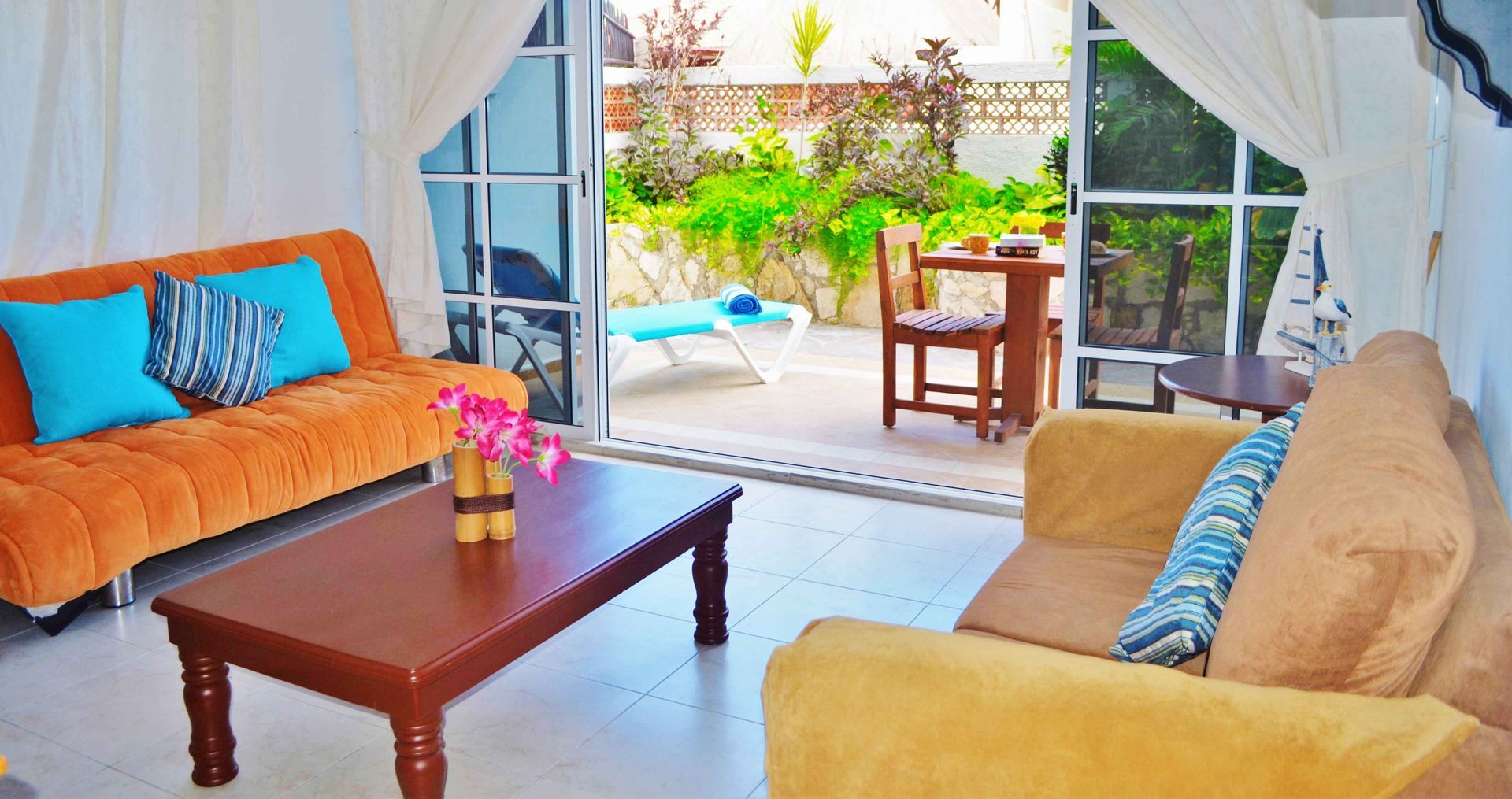 Sala de estar con puertas abiertas a un patio; sofás naranjas y beige.
