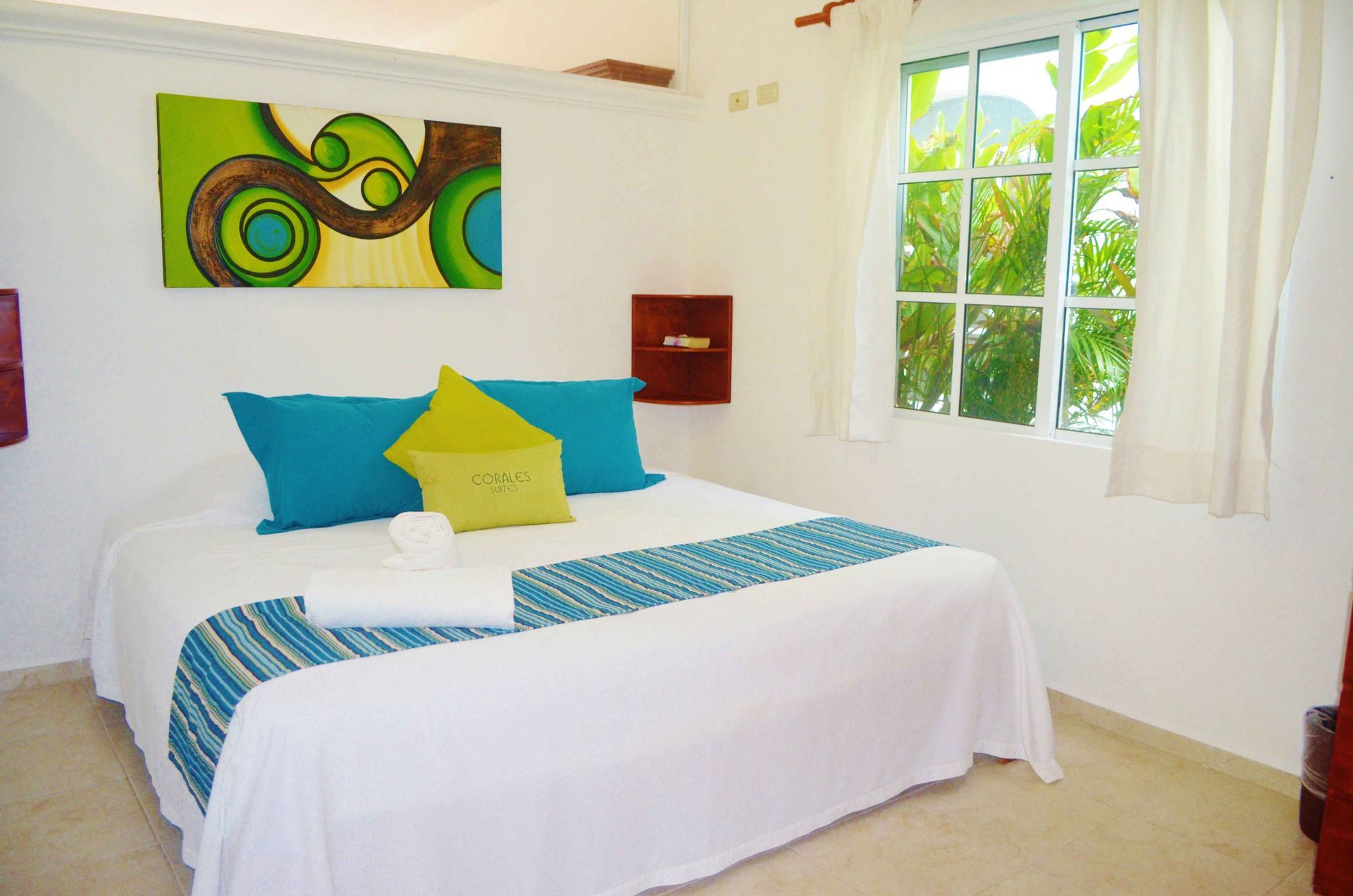 Dormitorio con cama blanca, almohadas verde azulado y verde lima, y ​​un cuadro abstracto encima de la cama.