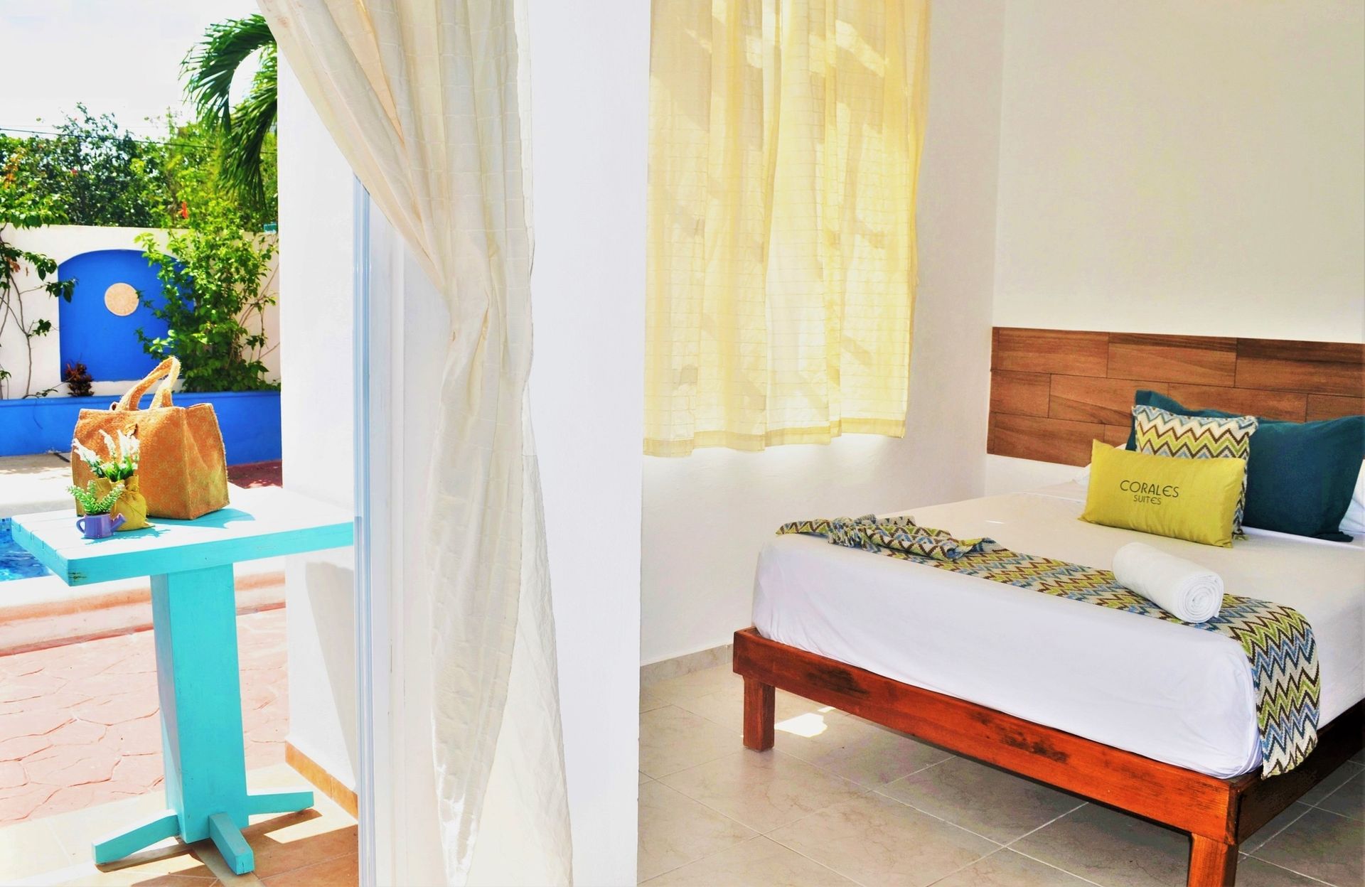 Dormitorio con cama y patio con una mesa turquesa con vistas a la piscina.