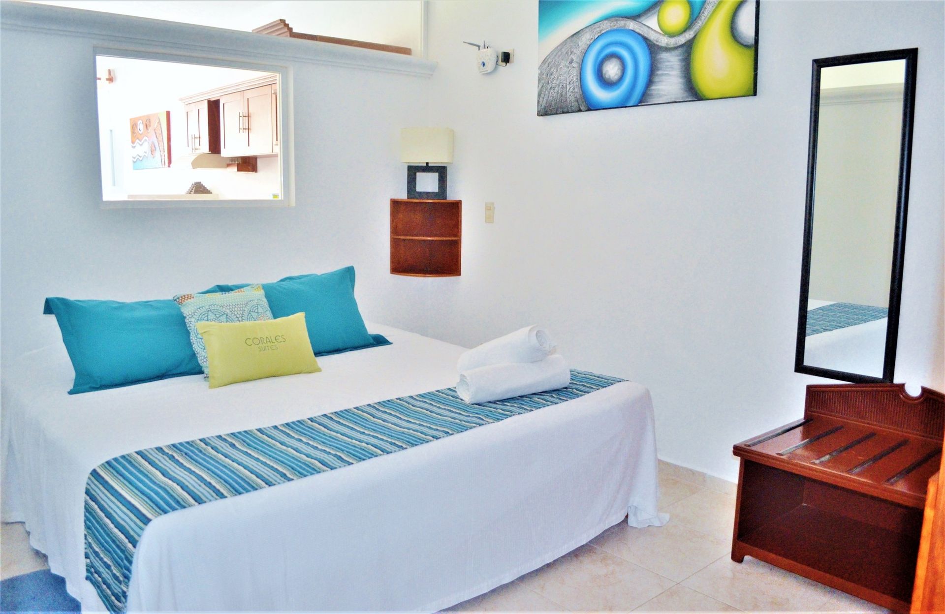 Dormitorio con paredes blancas, cama con almohadas color verde azulado y una alfombra azul.