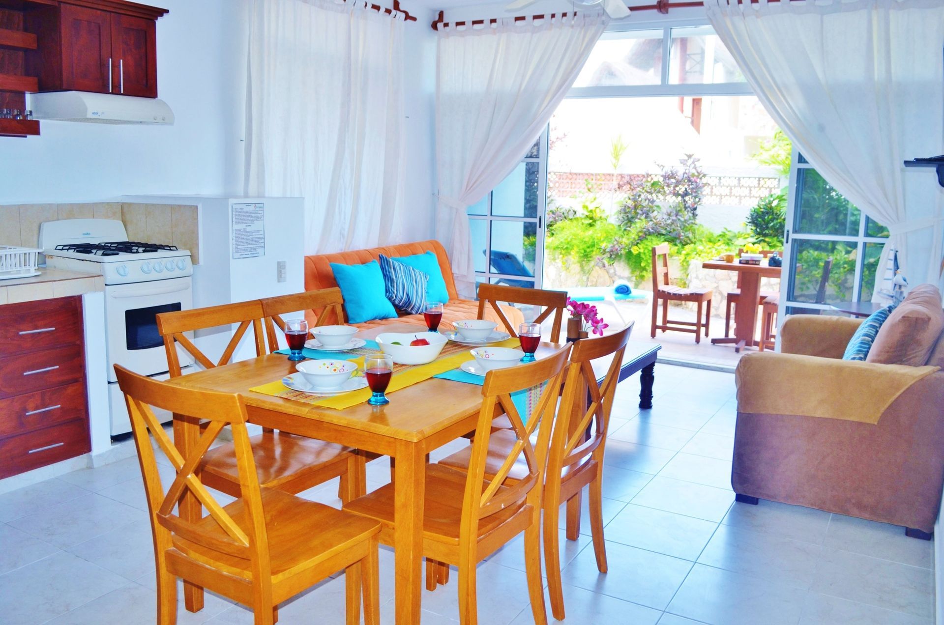 Dining area with a wooden table and chairs, kitchen, and open doors to a patio.