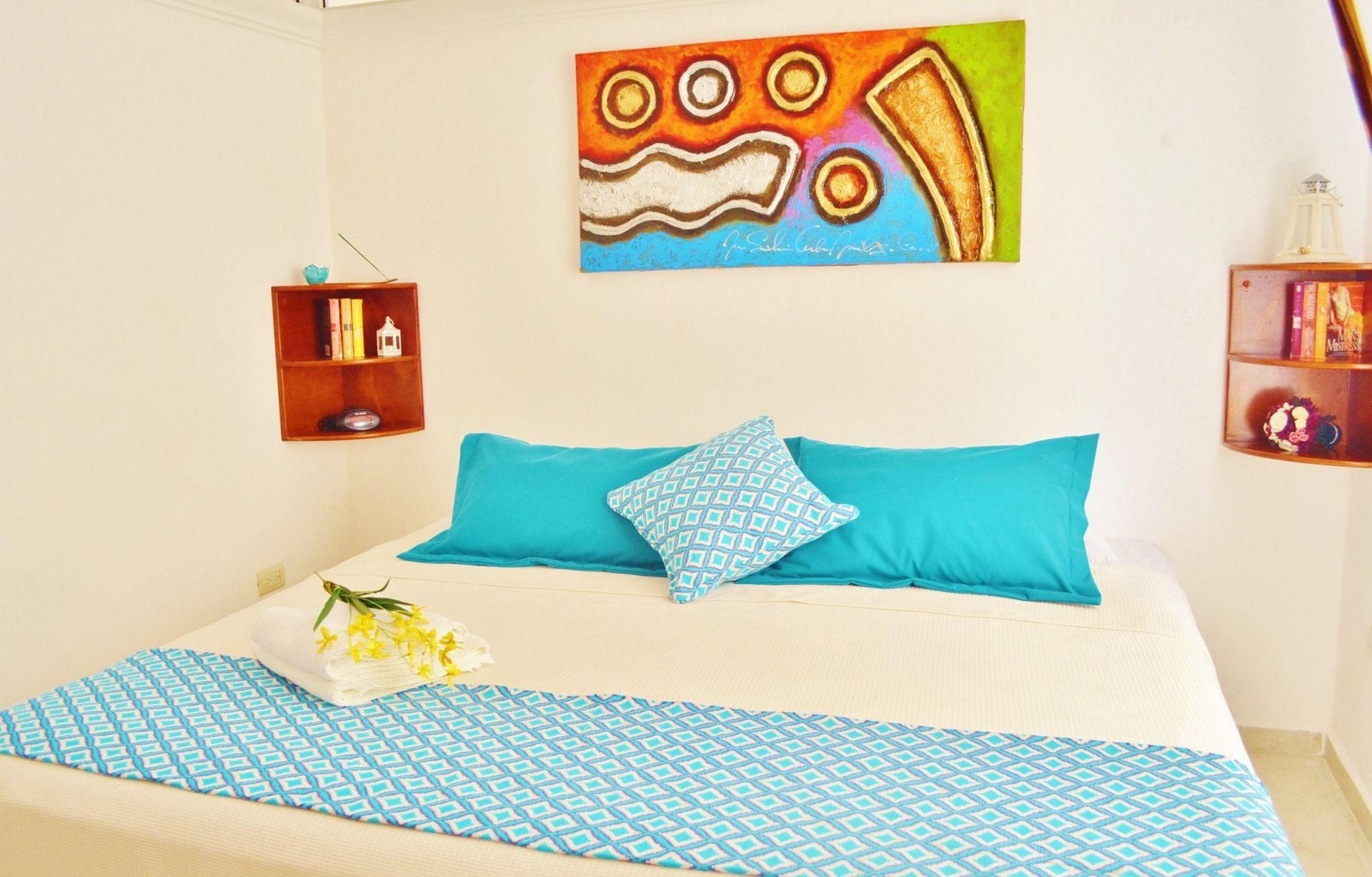 Dormitorio con cama blanca, cojines color verde azulado y una alfombra decorativa.