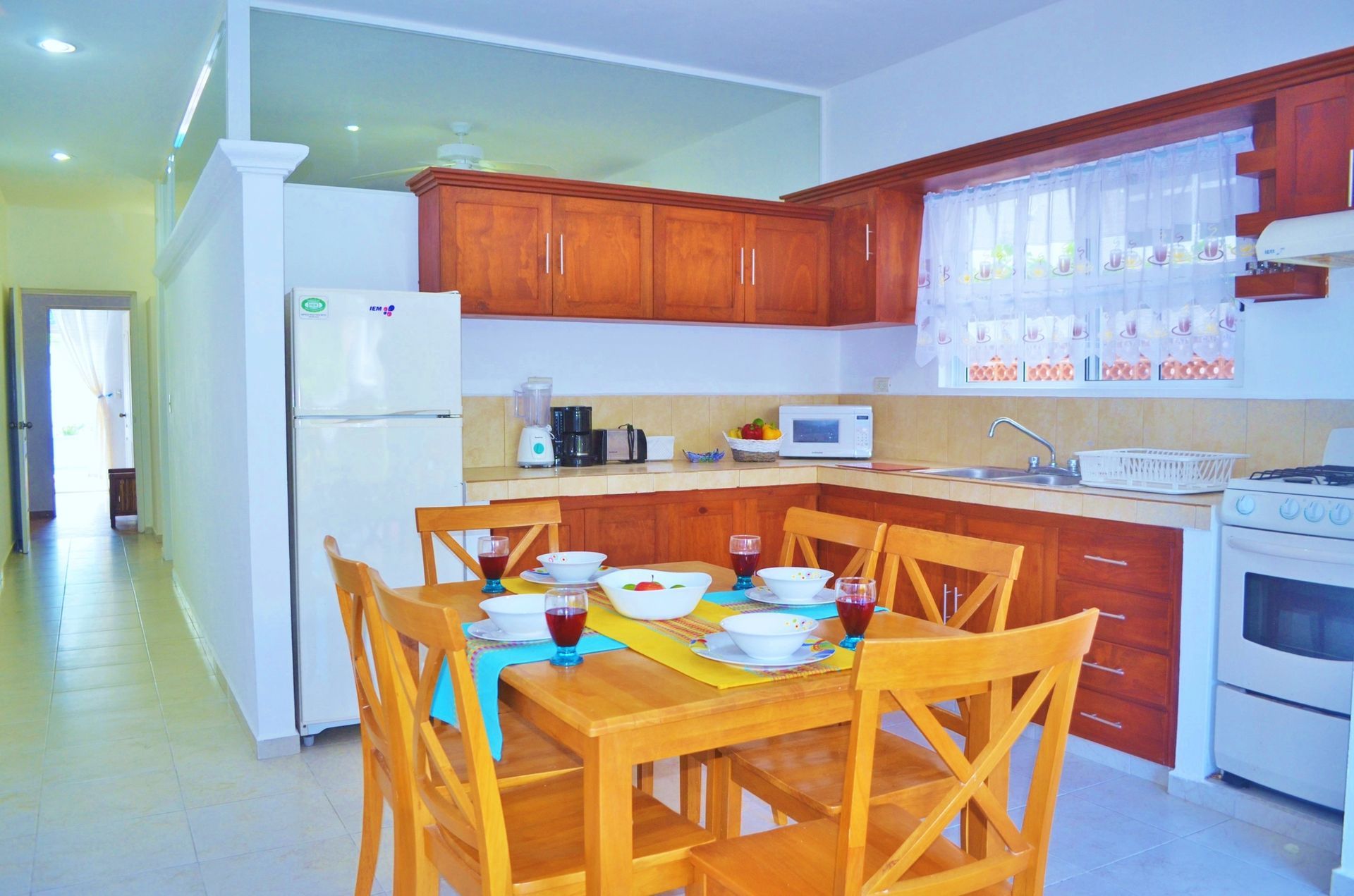 Cocina y comedor con armarios de madera, mesa puesta para comer y electrodomésticos.