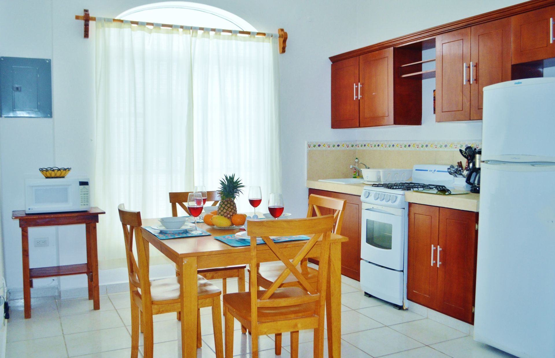 Cocina con mesa de comedor, armarios de madera y electrodomésticos blancos. Fruta y vino sobre la mesa.