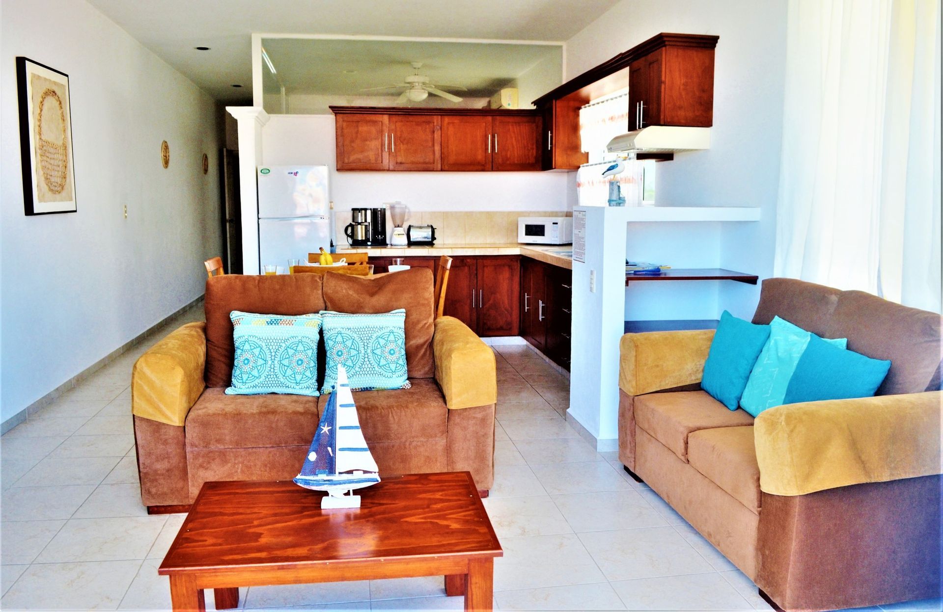 Cozy living area with brown sofa, teal pillows, wooden coffee table, and kitchen in the background.