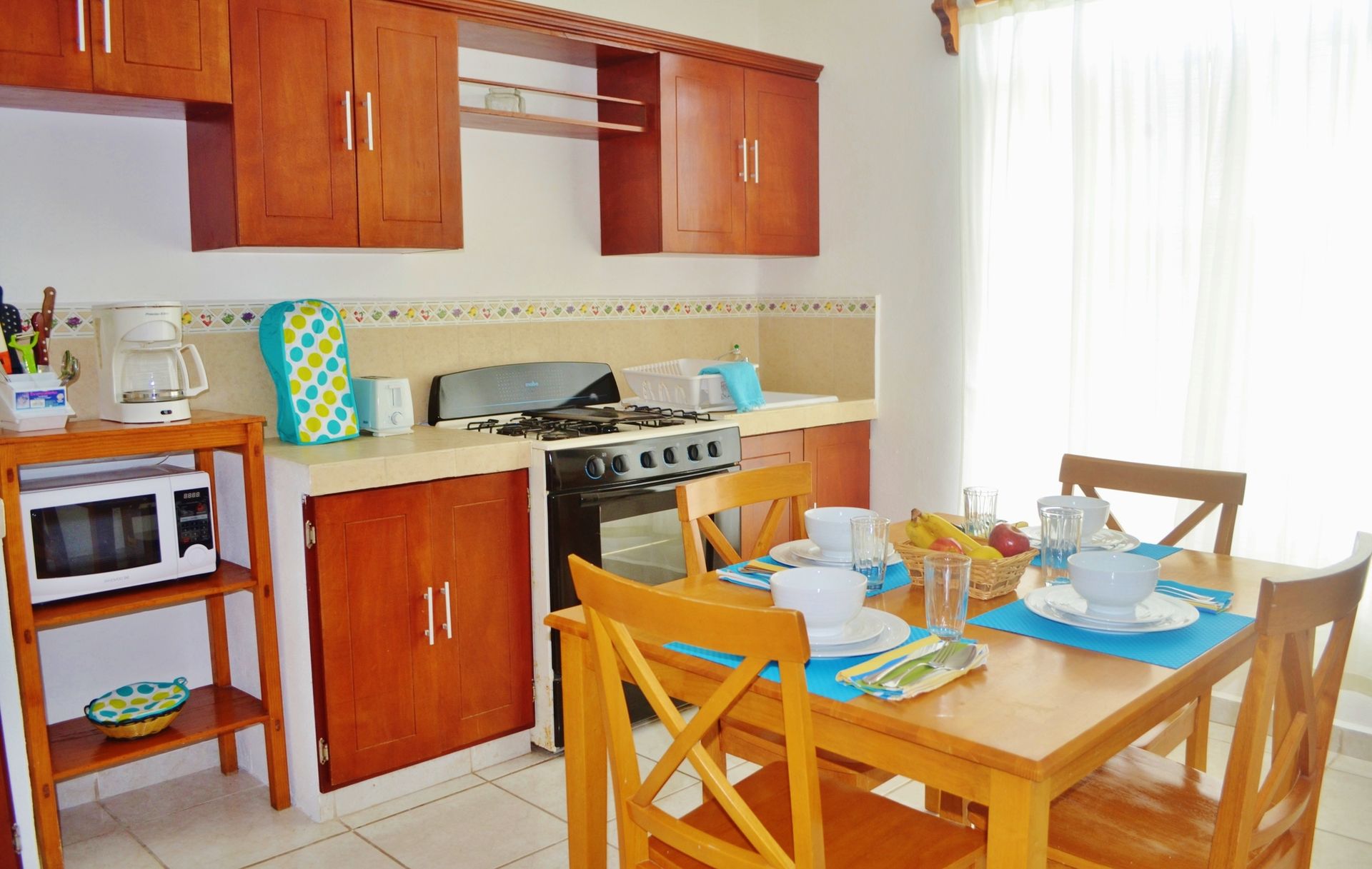 Cocina con armarios de madera, estufa, microondas y mesa de comedor puesta para comer.