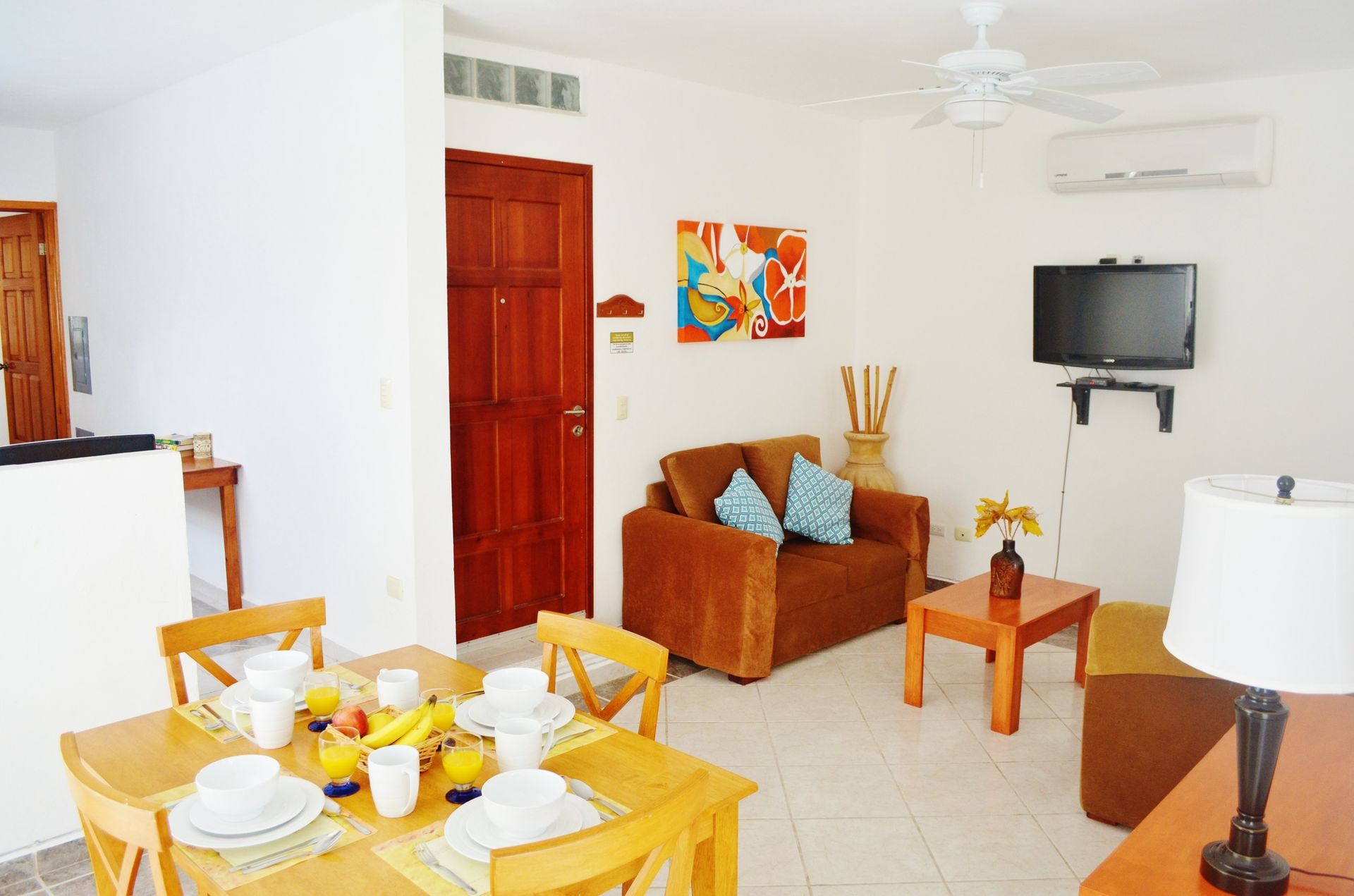 Dining area with breakfast set on a table, next to a living room with a brown couch and TV.