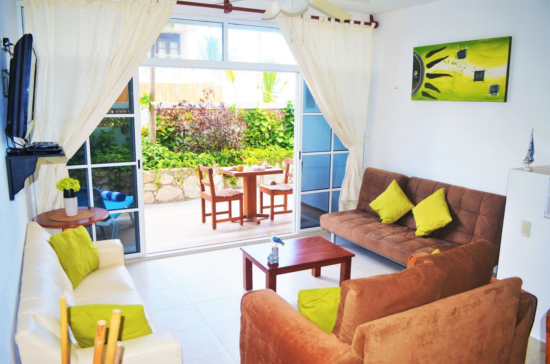 Living room with open doors to a patio. Brown and white furniture, green pillows, and colorful artwork.