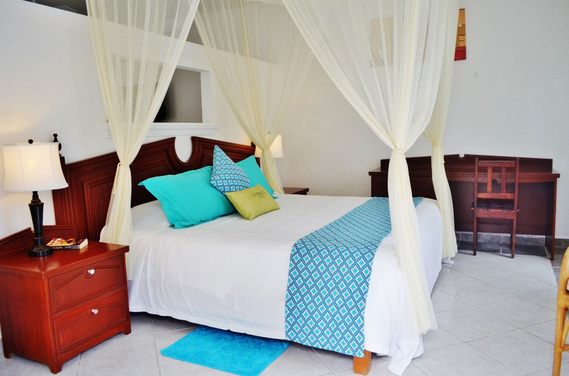 Bedroom with canopy bed, white bedding, turquoise accents, mahogany nightstand, and desk.