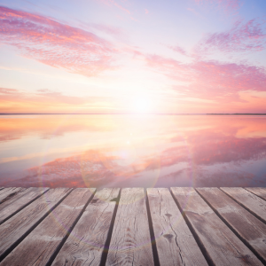 Wooden dock facing a calm pastel sunrise over water with pink and orange clouds