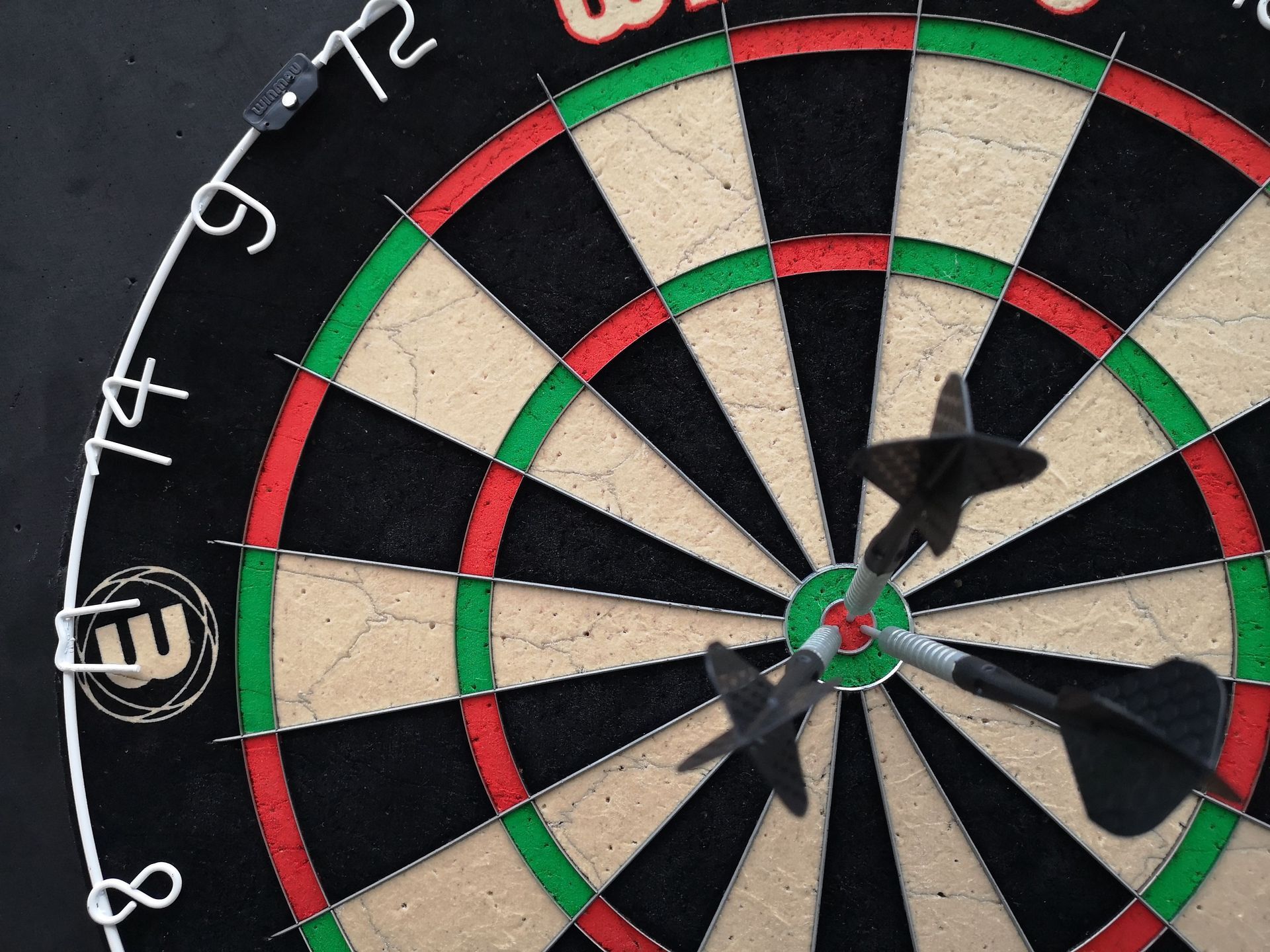 Dartboard with several darts embedded, showing red, green, black, and cream scoring rings.