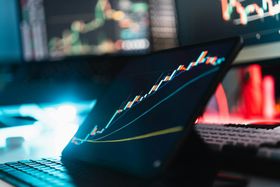Laptop with glowing stock charts in a dim trading workspace, lit by blue and red screens