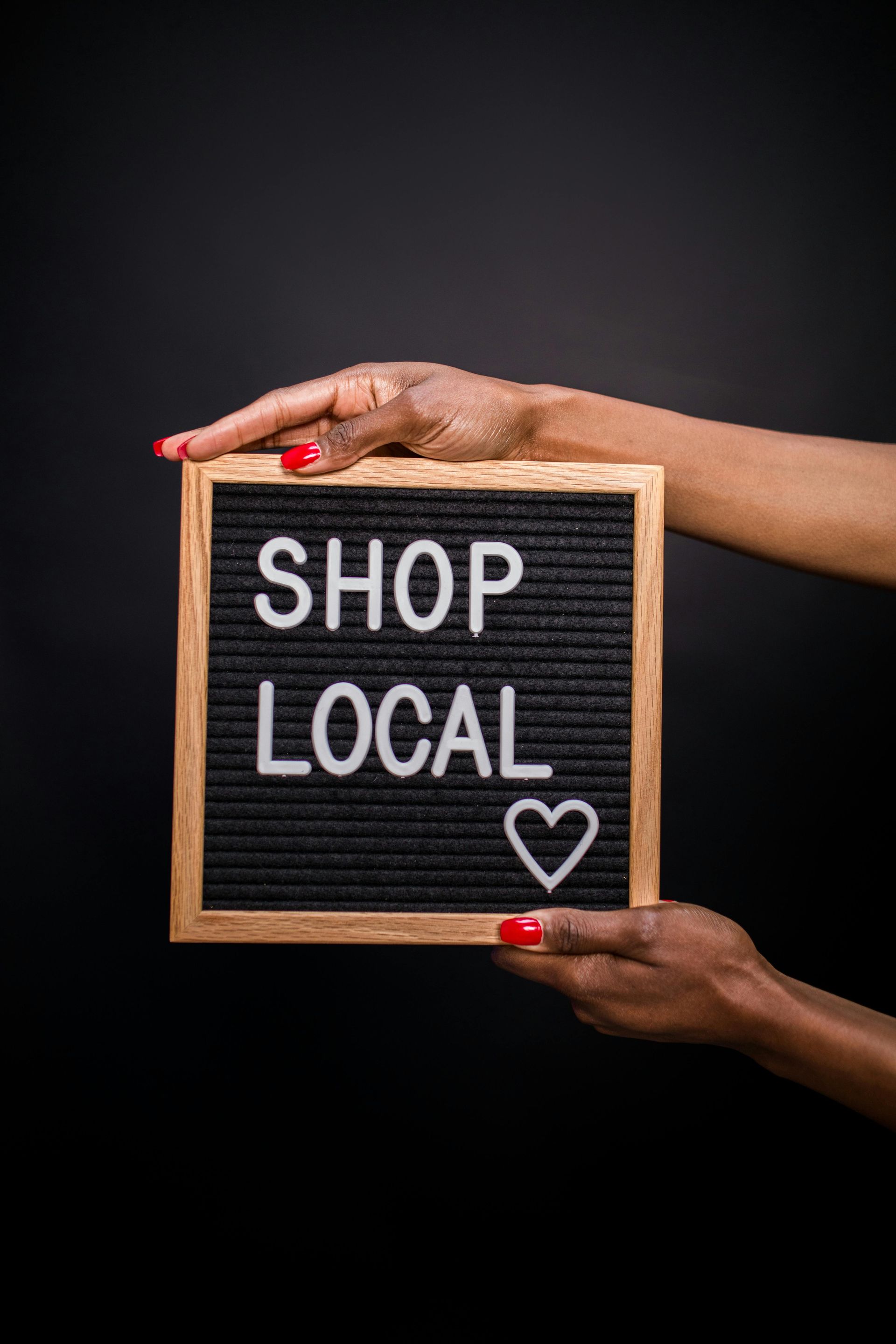 Hands holding a small chalkboard sign that says “SHOP LOCAL” with a heart on a black background