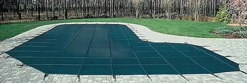 A green pool cover is sitting on top of a brick patio.