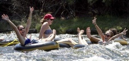 People floating in inner tubes on a river, raising arms and making peace signs.