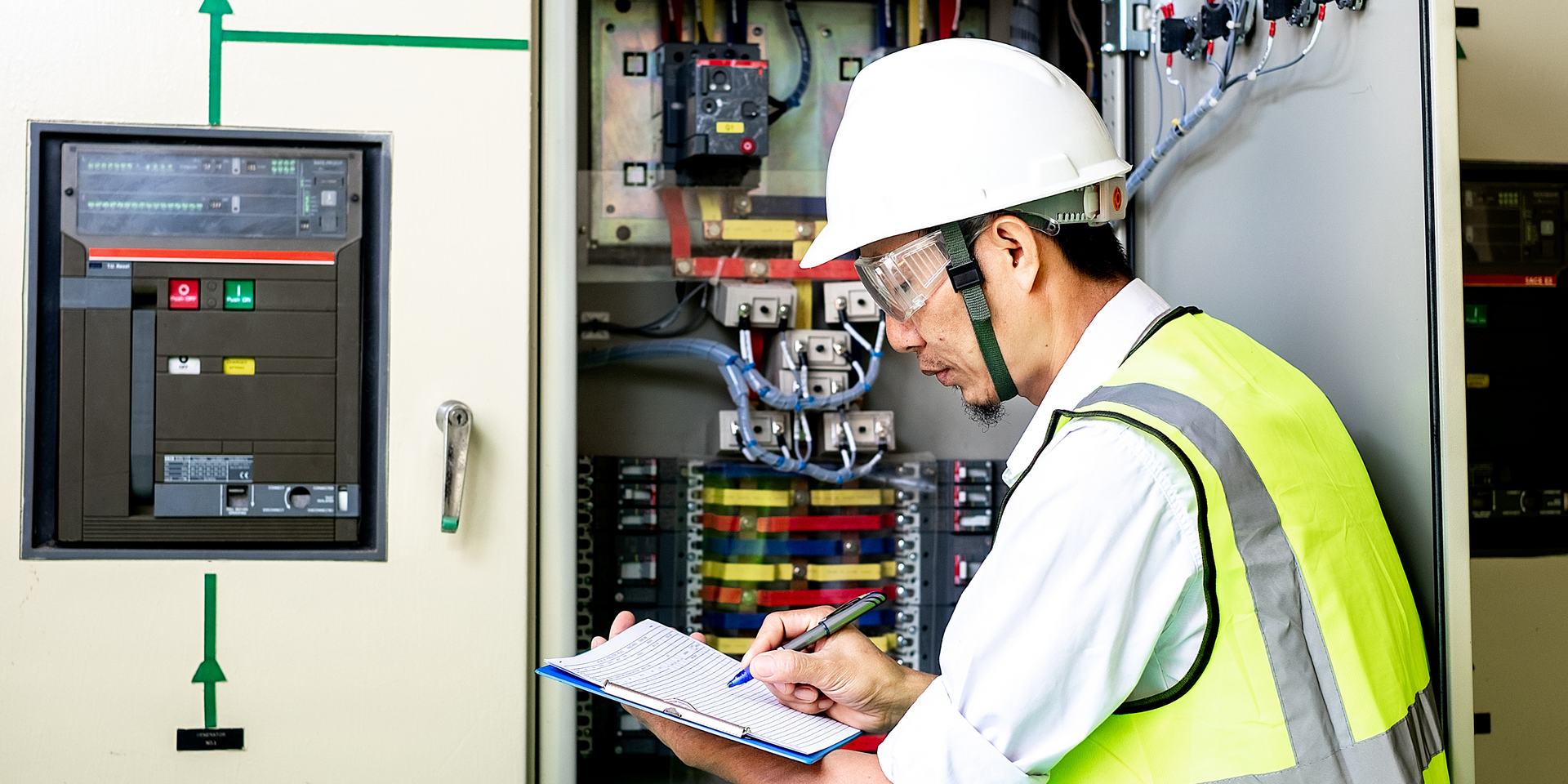 Electrician with white helmet in front of switchboard with clipboard