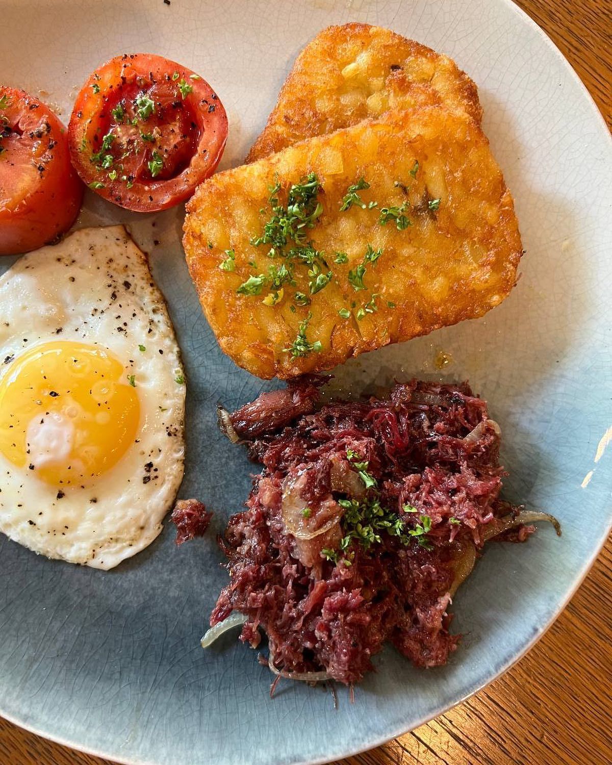 Breakfast plate: fried egg, tomato slices, hash browns, corned beef hash.
