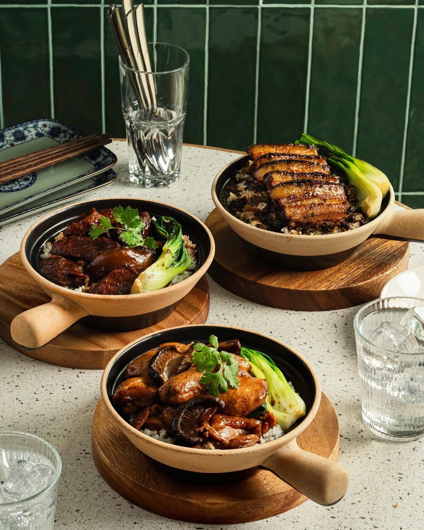 Three bowls of Asian food with rice, meat, and greens on a table.
