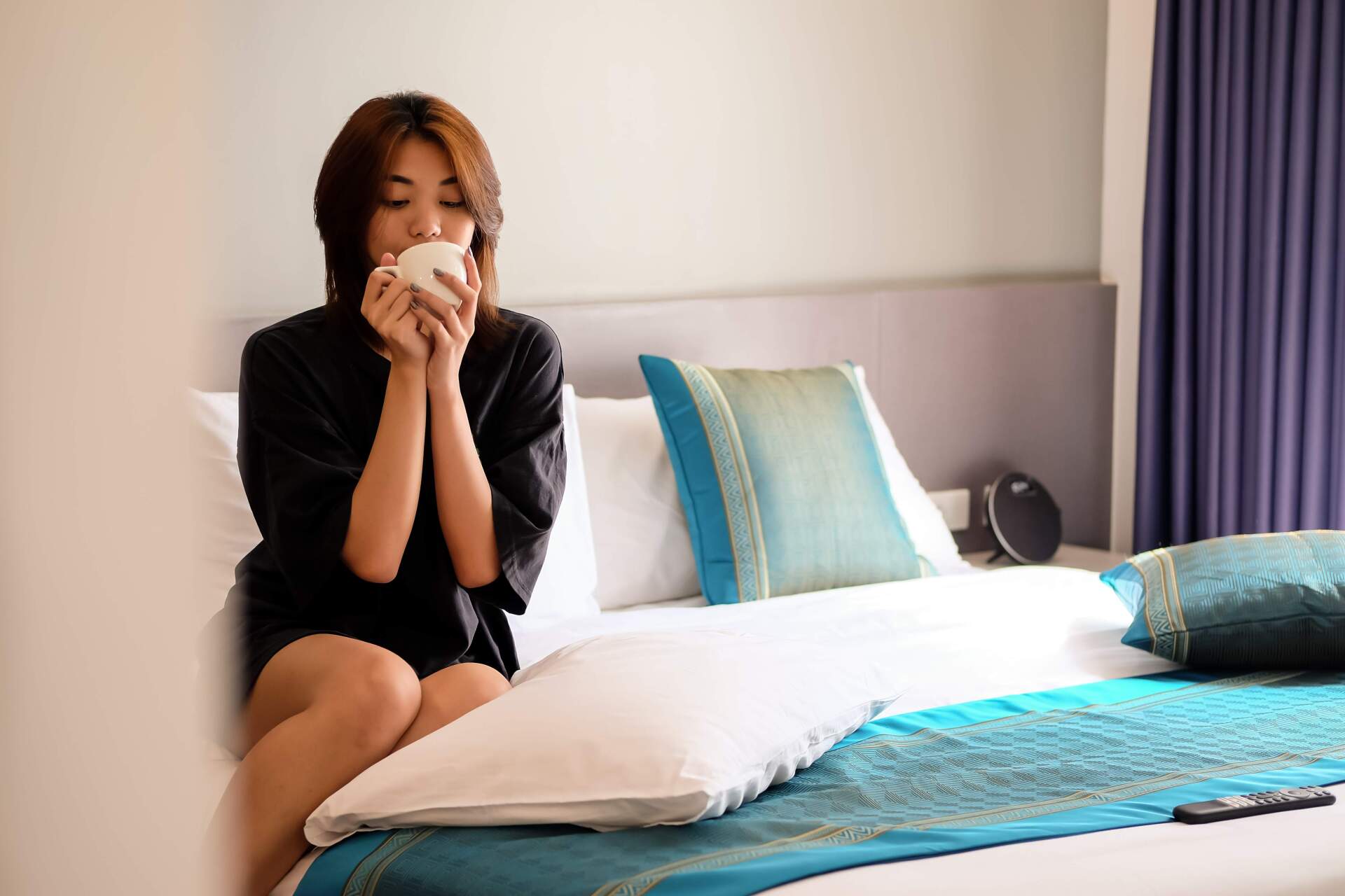 Woman sipping morning coffee on hotel bed at The Belamy House Makati