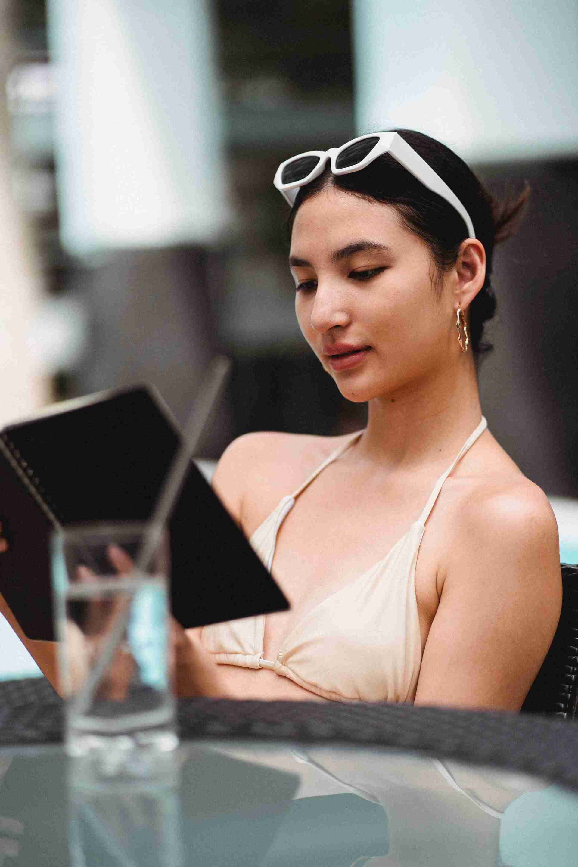 Woman in a beige dress reading a menu at an outdoor café, with sunglasses on her head.