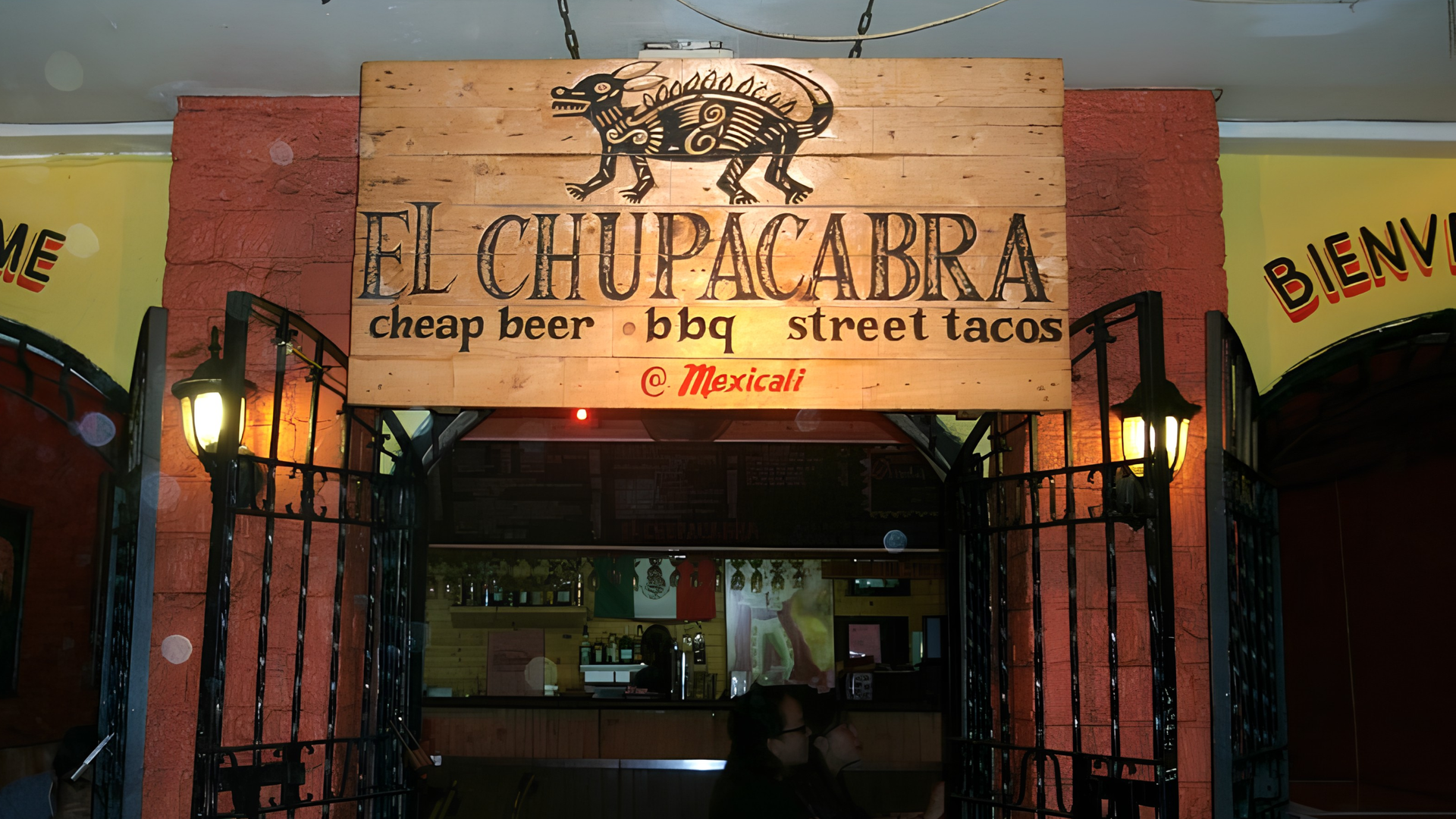 Storefront sign reading “El Chupacabra,” with “cheap beer” and “street tacos” on a warmly lit entrance.