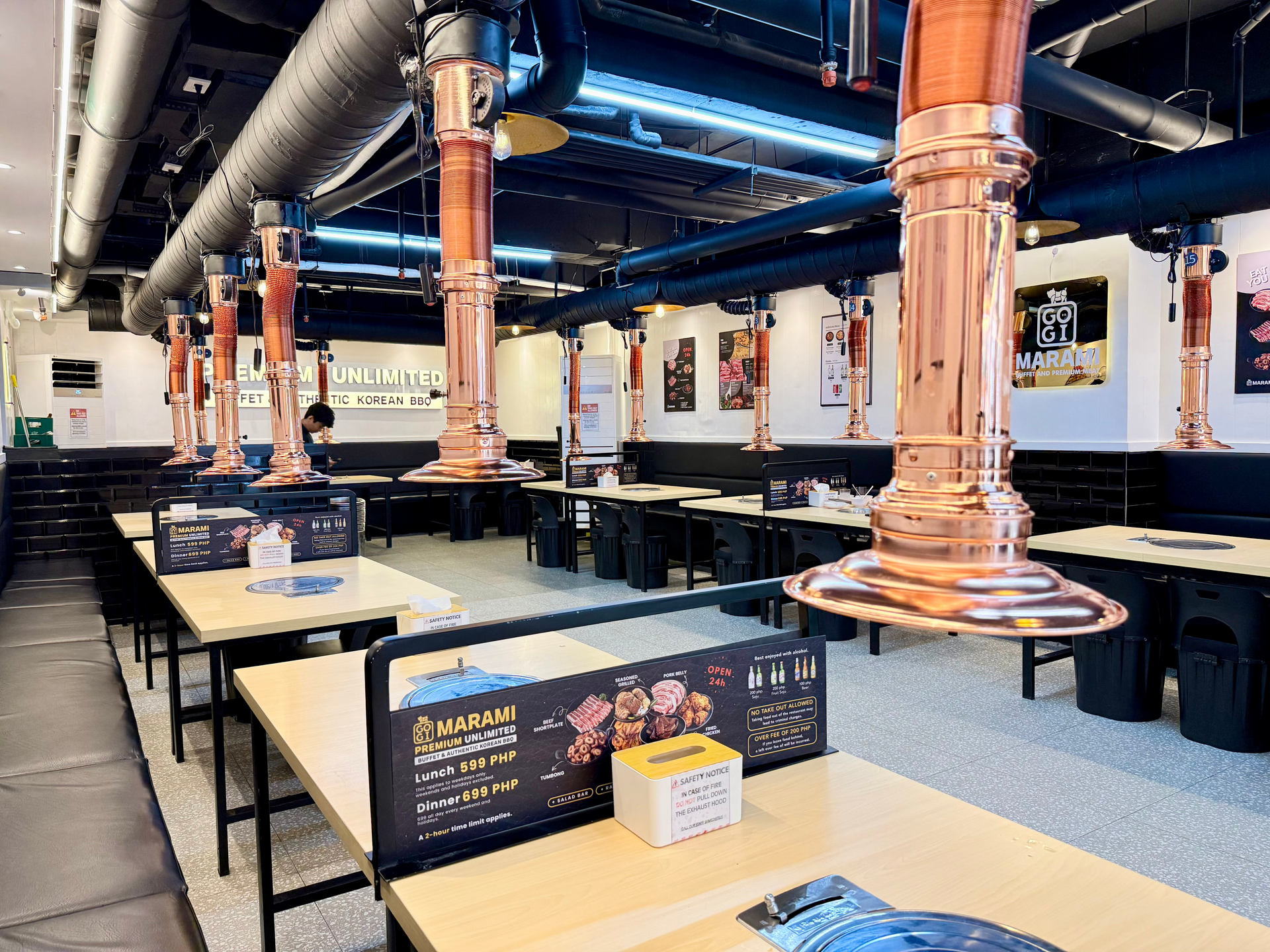 Modern restaurant dining area with black tables, orange ductwork, and hanging lights at an indoor venue