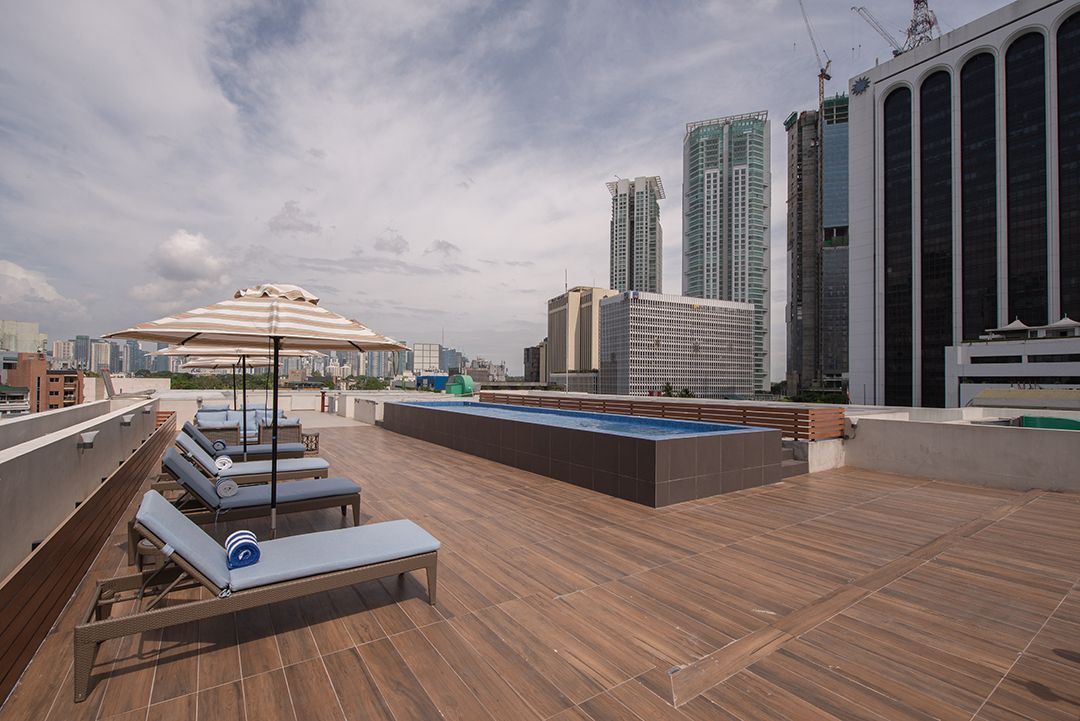 Rooftop pool deck with lounge chairs, umbrellas, and city skyscrapers under a cloudy sky