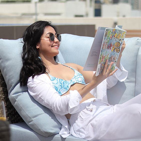 A woman in a bikini laying on a couch reading a book 