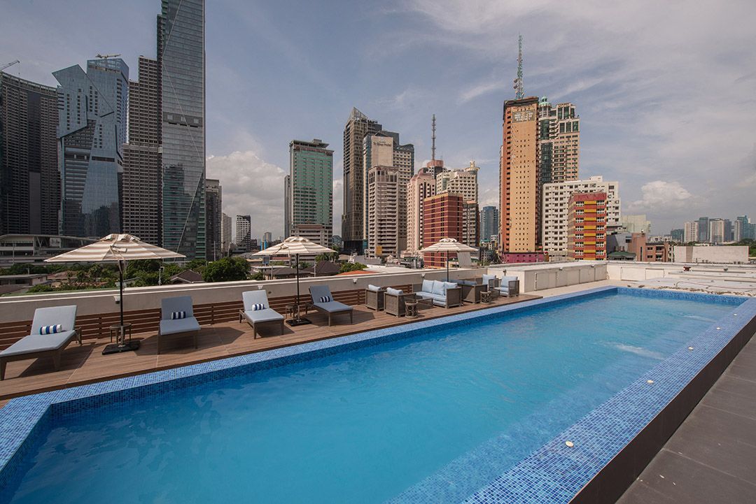 A large swimming pool on top of a building with a city skyline in the background.