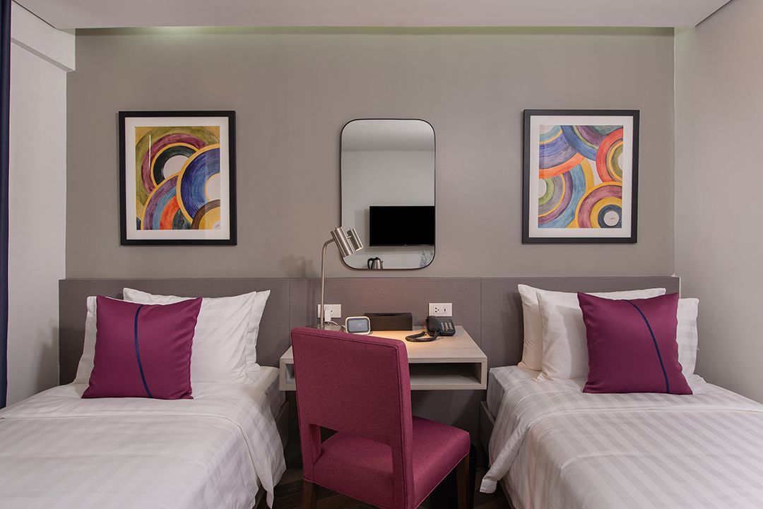 Twin bed hotel room with colorful wall art at The Belamy House Makati