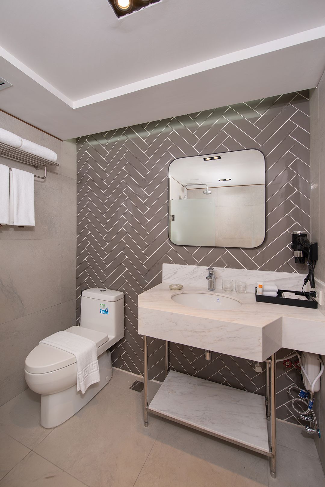 Modern hotel bathroom with marble vanity and herringbone tile wall