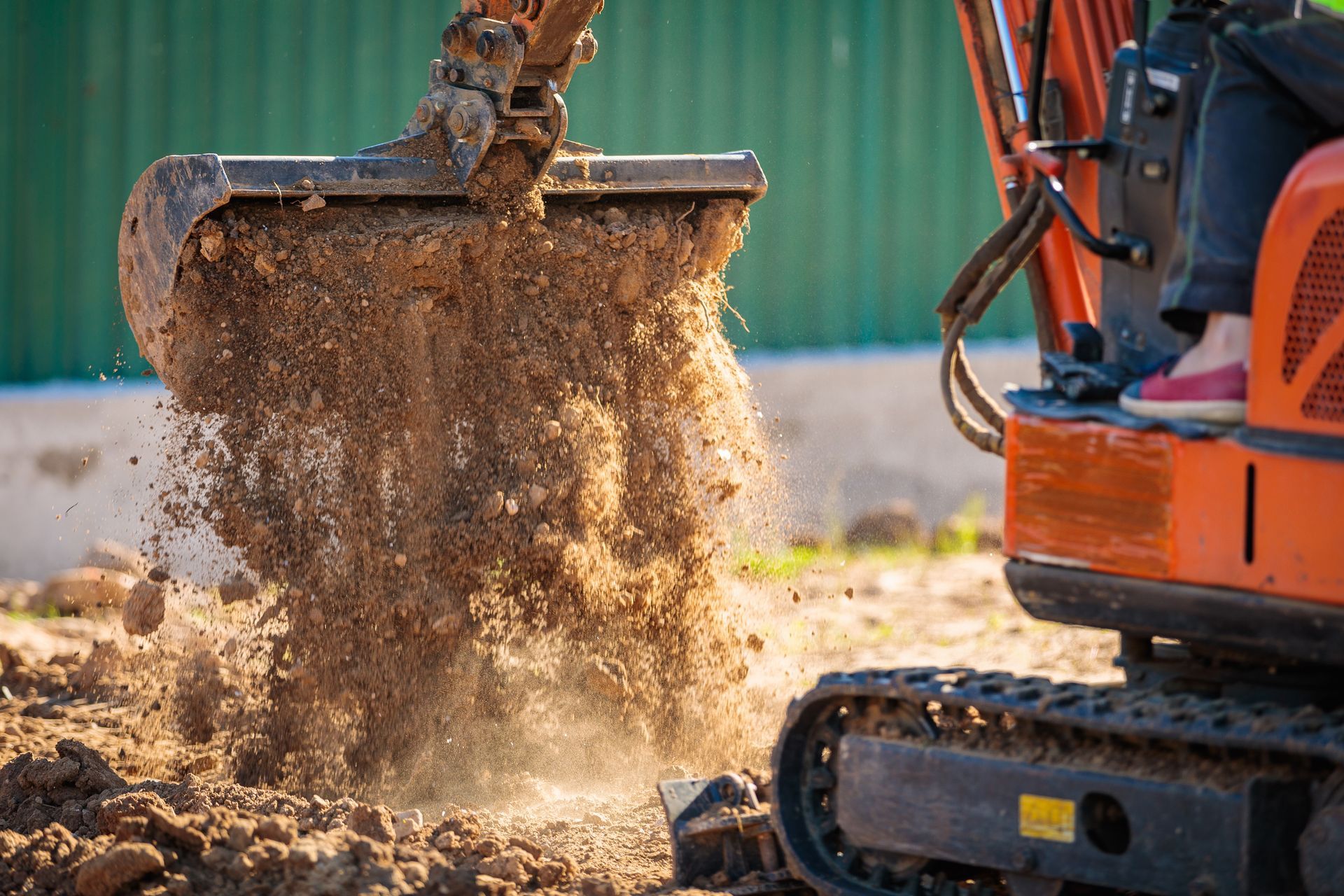 Orange excavator dumping dirt, close-up, outdoors.