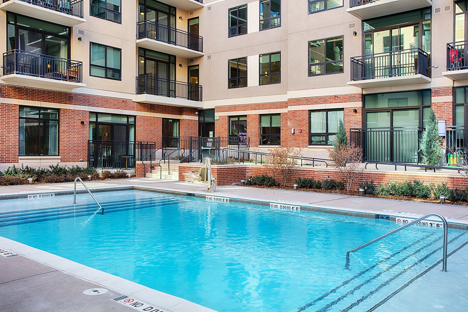 Swimming pool in a courtyard surrounded by a multi-story brick and stucco building with balconies and windows.