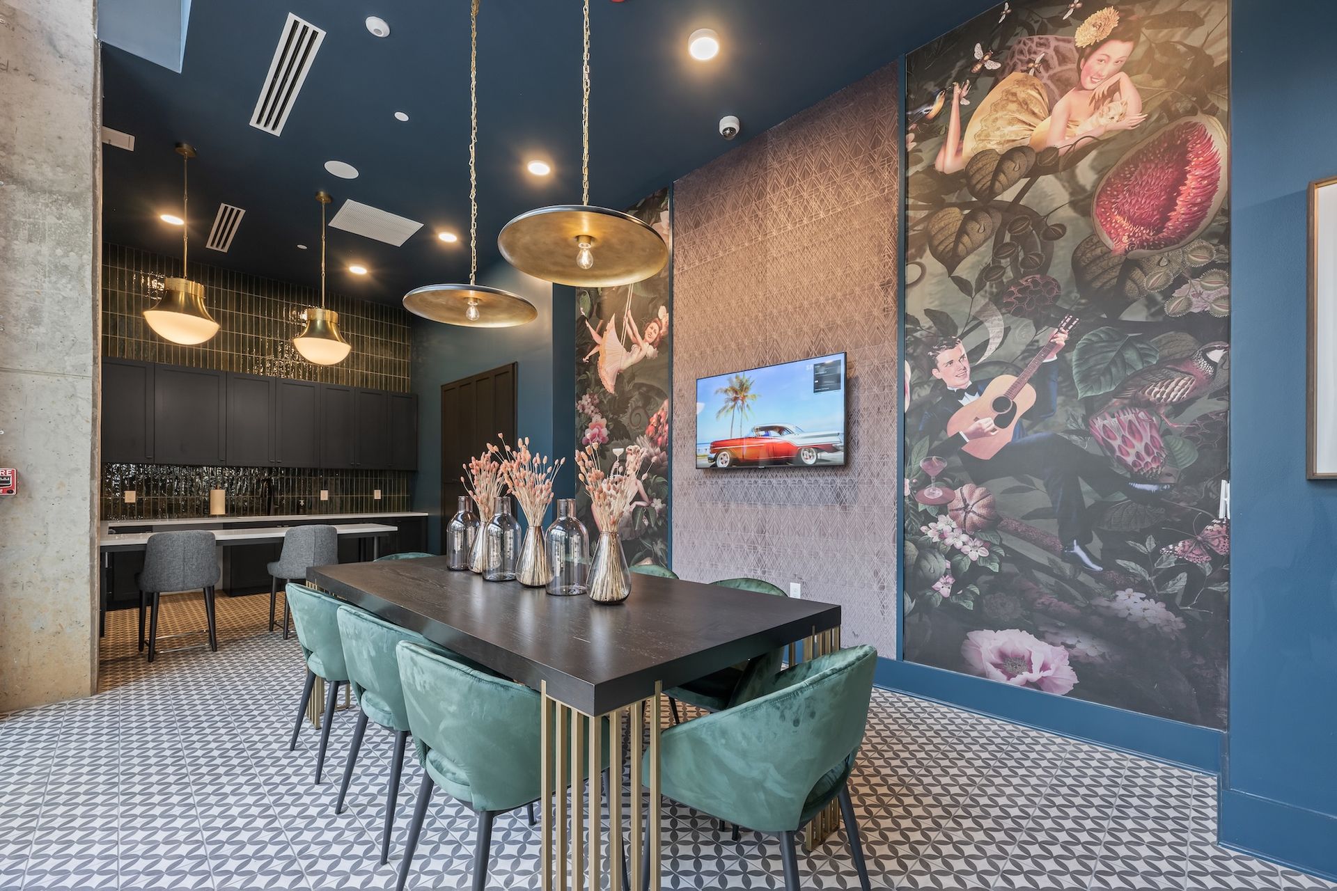 A modern dining area with a dark table, green chairs, floral wall, and a TV.