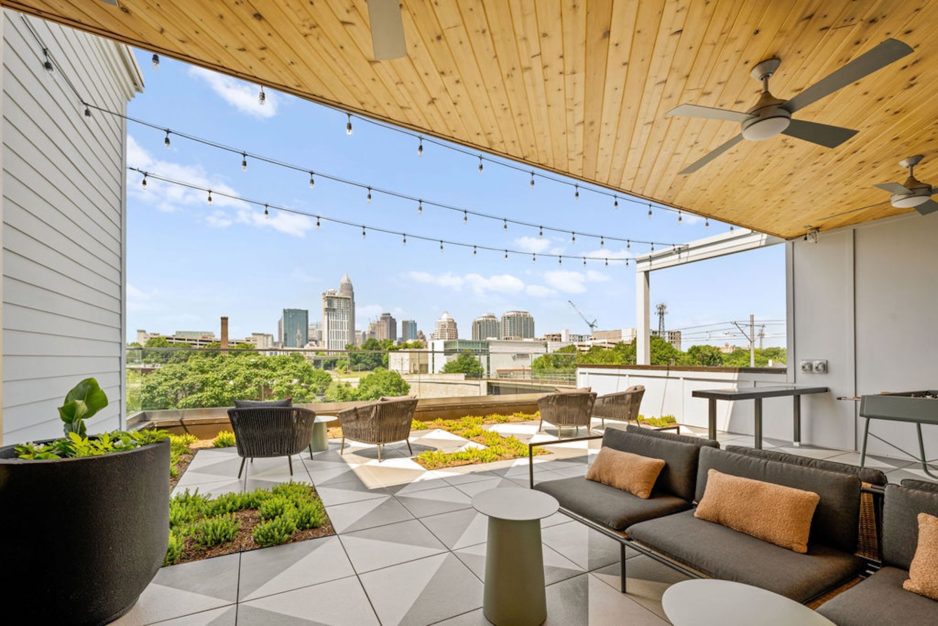 Rooftop patio with cityscape view, gray and white tiled floor, seating areas, string lights, and wooden ceiling.