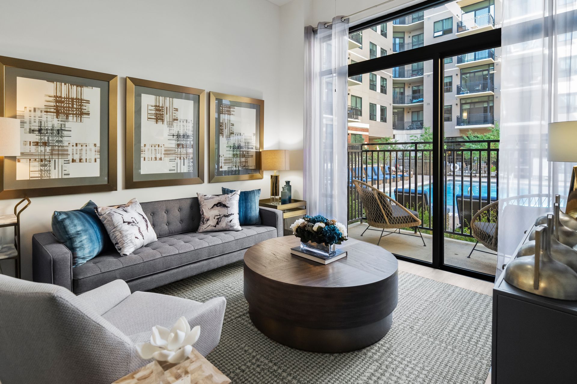 Living room with gray sofa, round coffee table, balcony with pool view, artwork.