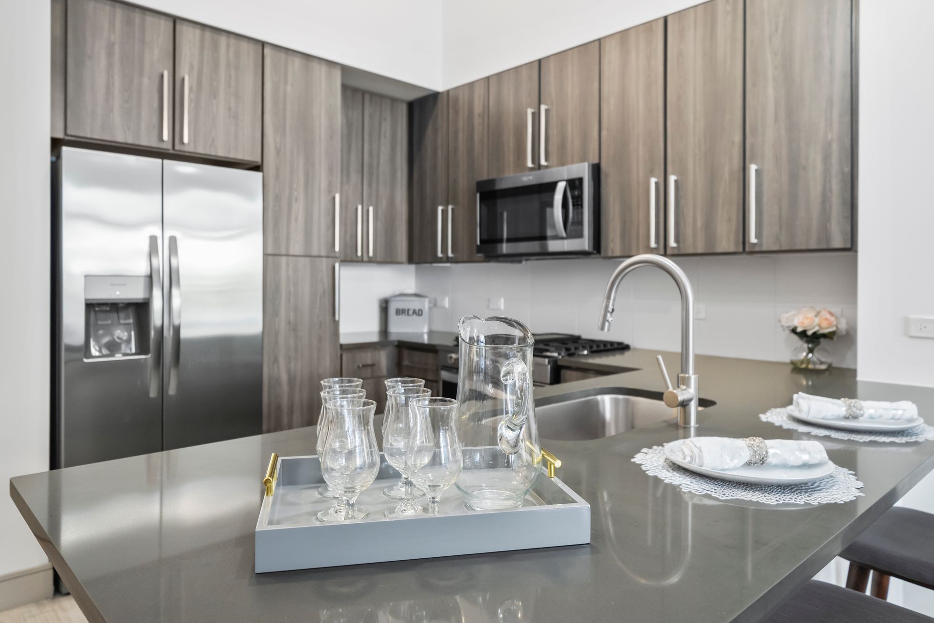 Modern kitchen with stainless steel appliances, gray cabinets, and a gray island with glassware.