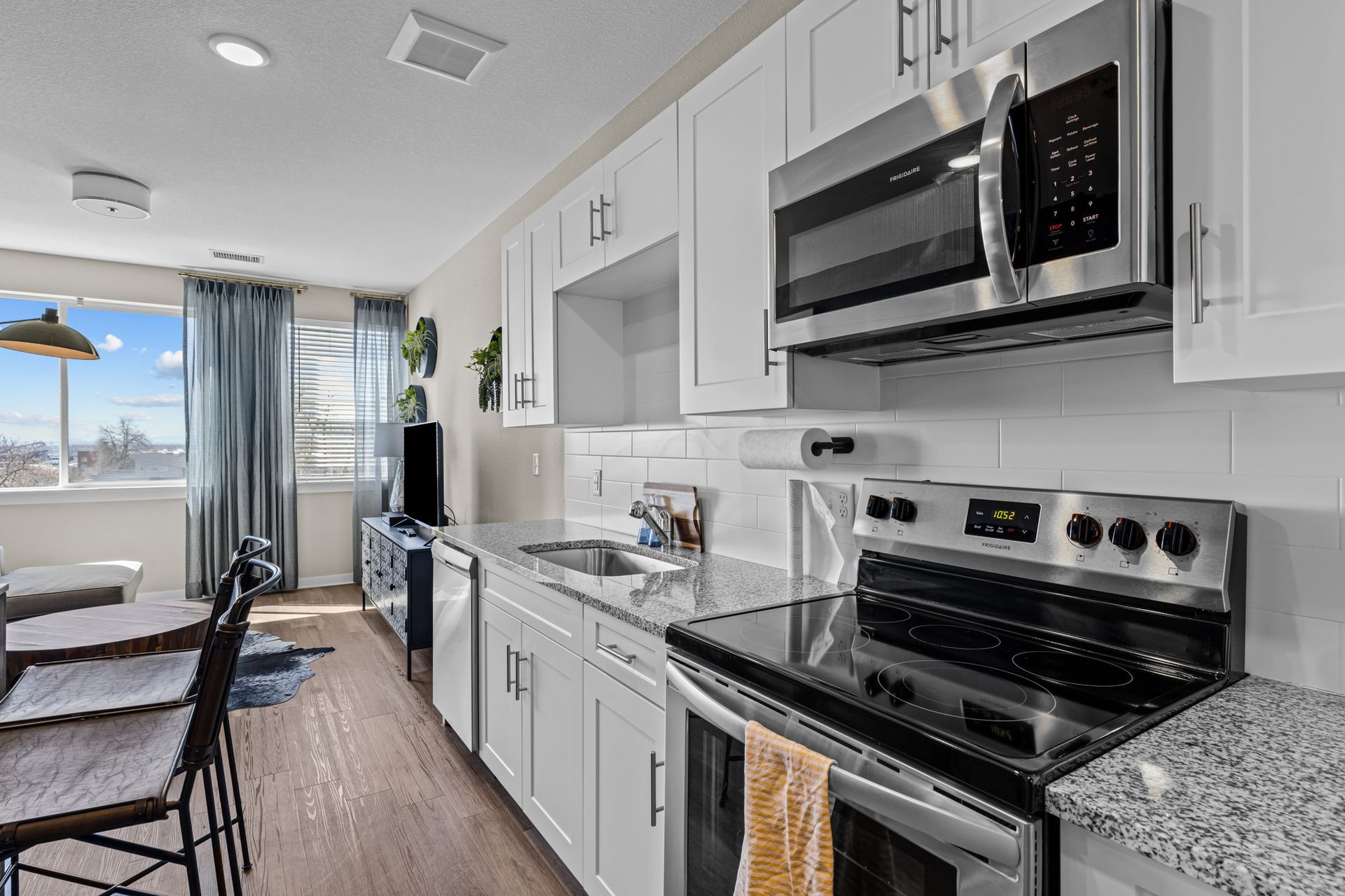 Modern kitchen with white cabinets, stainless steel appliances, and a window with curtains.