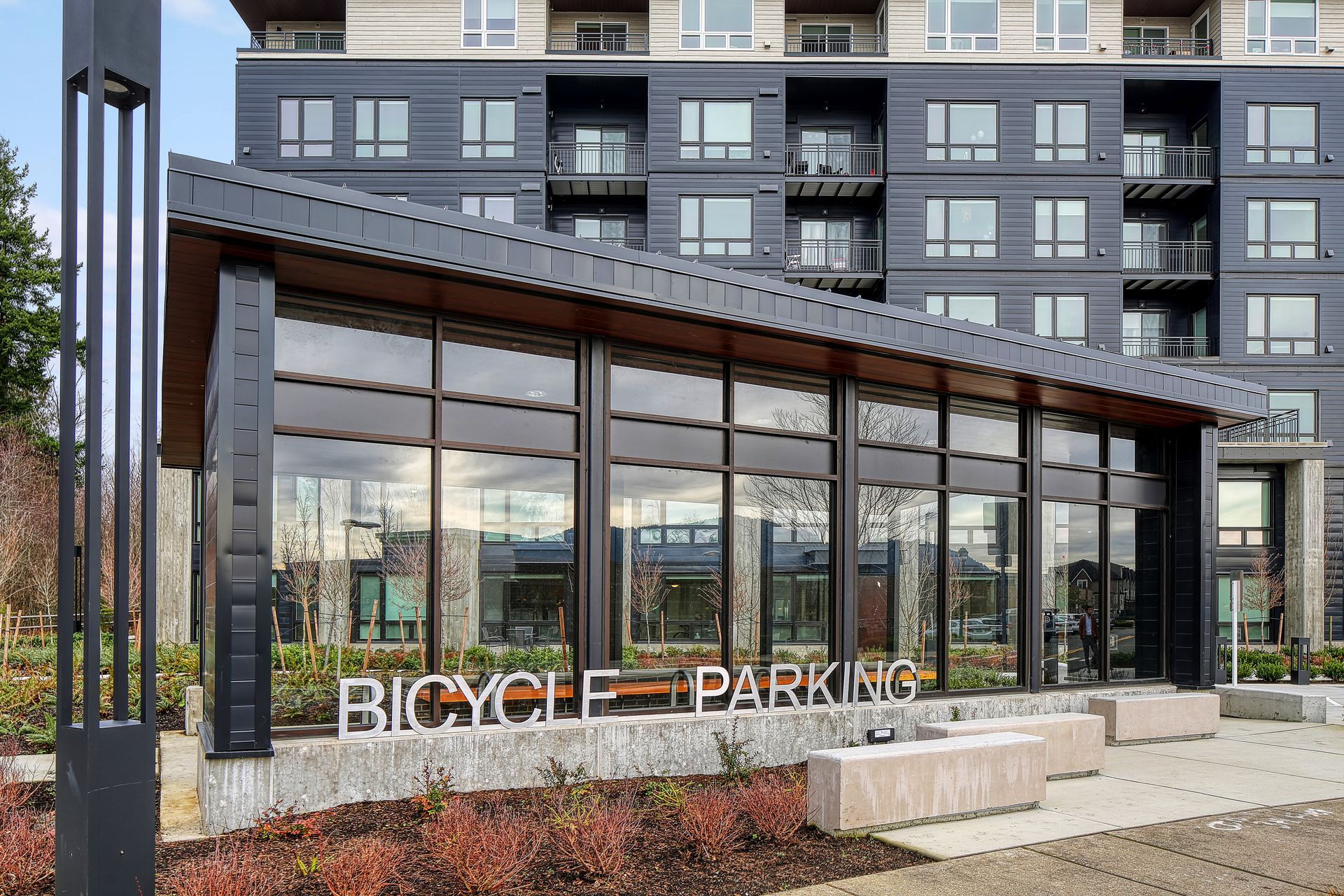 Bicycle parking shelter with large windows, near an apartment building.